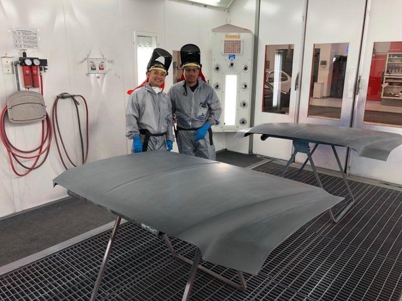 Two men are standing next to each other in a paint booth