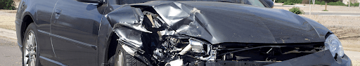 A car with a damaged front end is parked on the side of the road.
