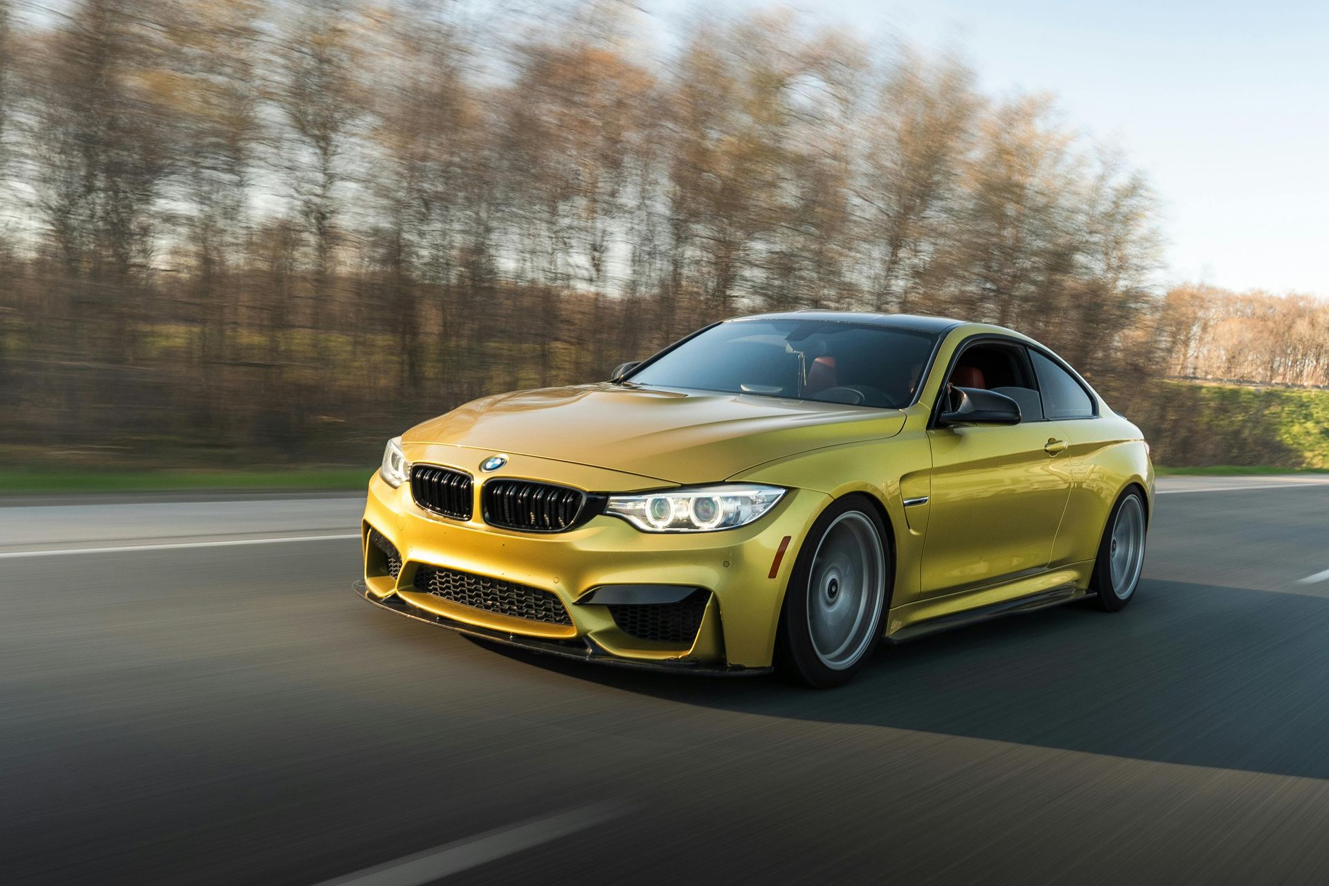 A yellow bmw m4 is driving down a road