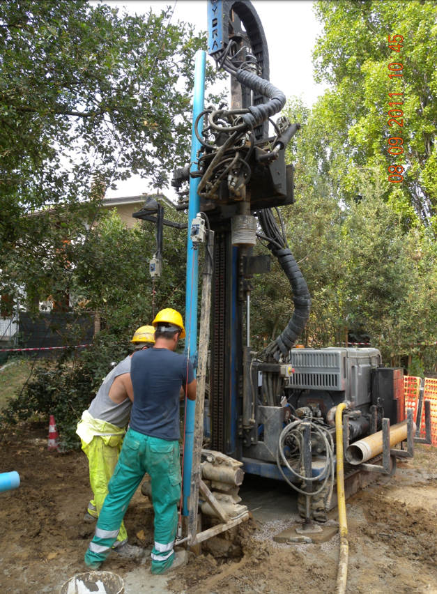 Operai che effettuano perforazioni in un cantiere edile accanto a una grande piattaforma e ai tubi flessibili.