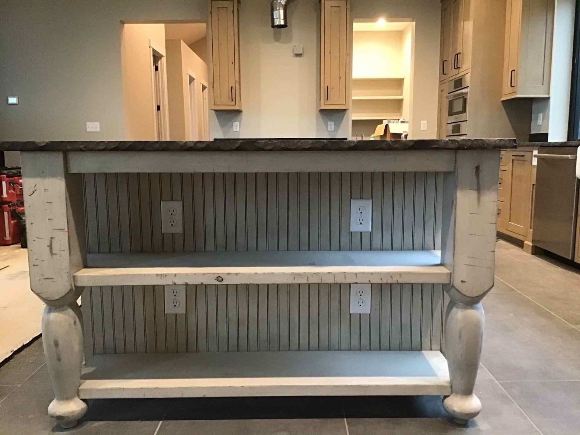 Kitchen island with distressed white finish, dark countertop, and two shelves.