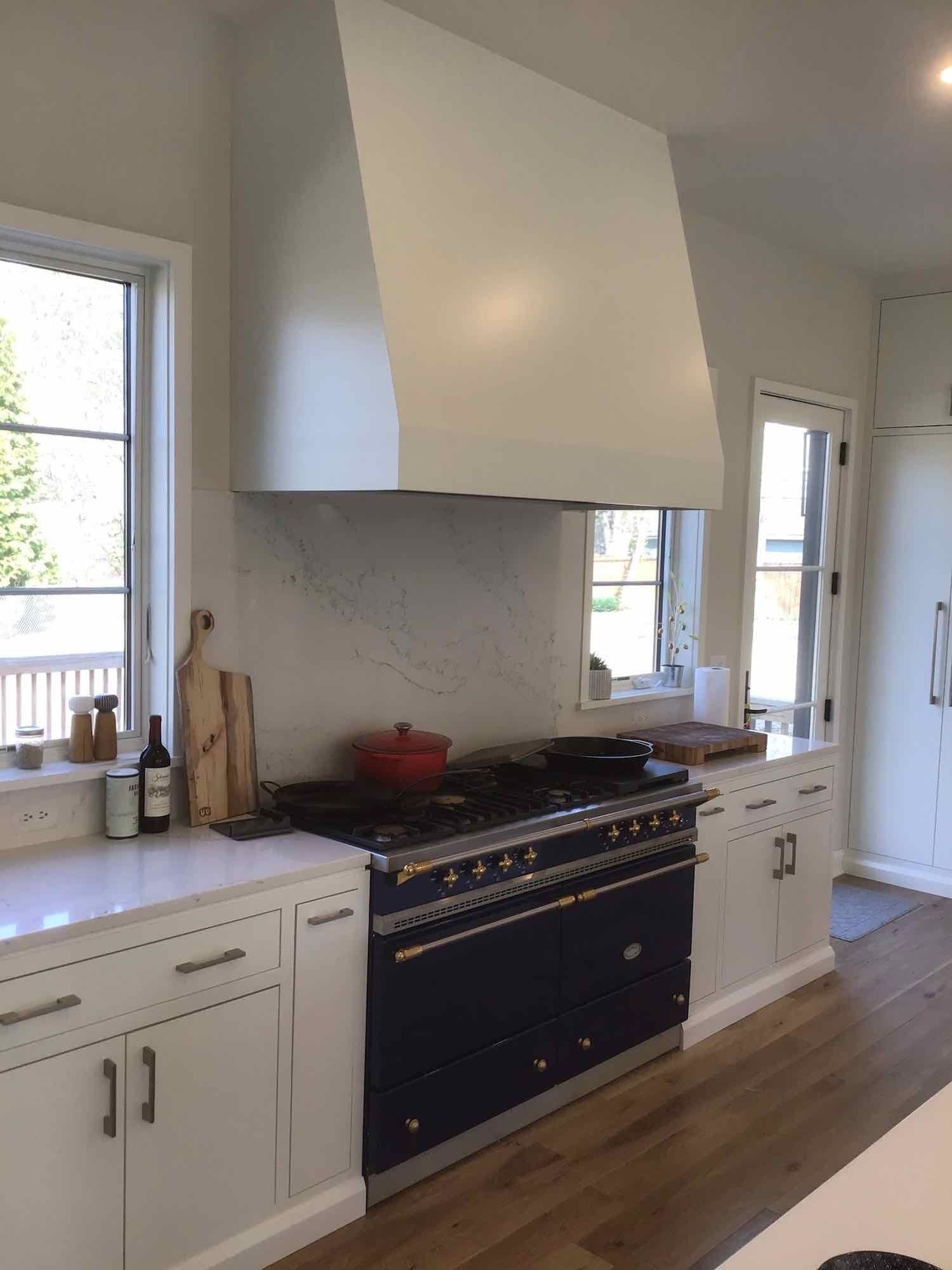 White kitchen with a navy blue range, white hood, and wooden floors.