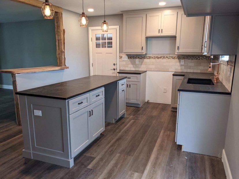 Gray kitchen with island, cabinets, and dark countertops, wood flooring. Two pendant lights hang.