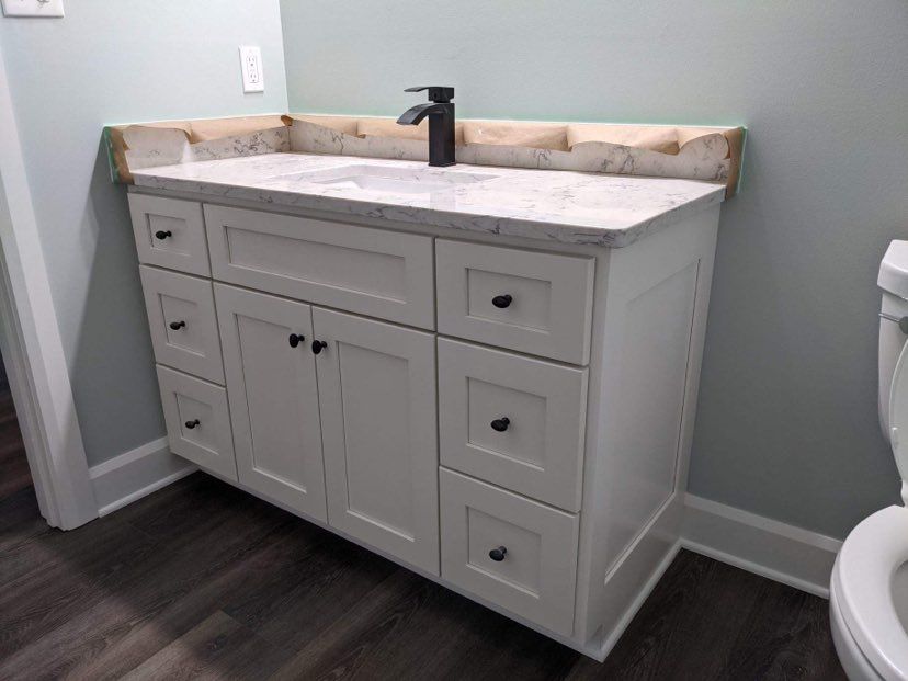 White bathroom vanity with dark hardware, marble countertop, and black faucet.