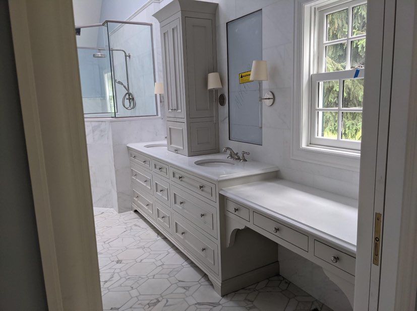 Bathroom with gray vanity, tall cabinet, marble countertops, and a window.