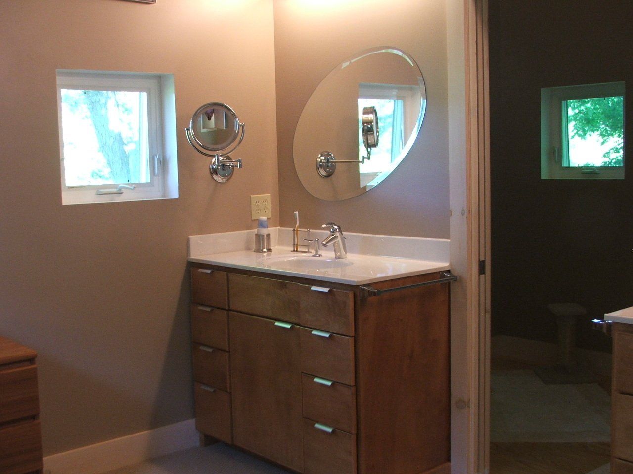 Bathroom with vanity, oval mirror, small window, and open doorway.
