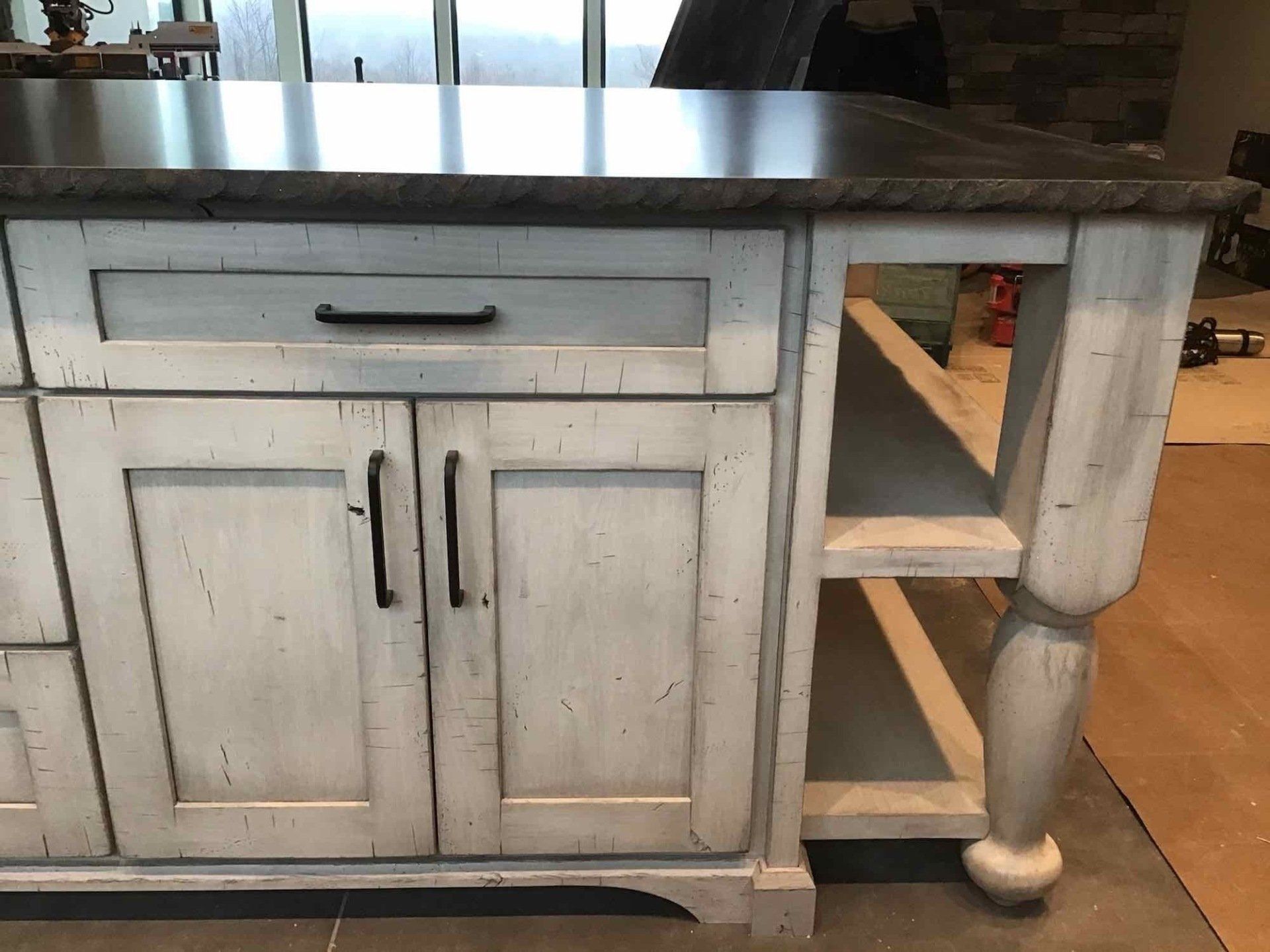 White distressed kitchen island with a dark countertop and open shelving.