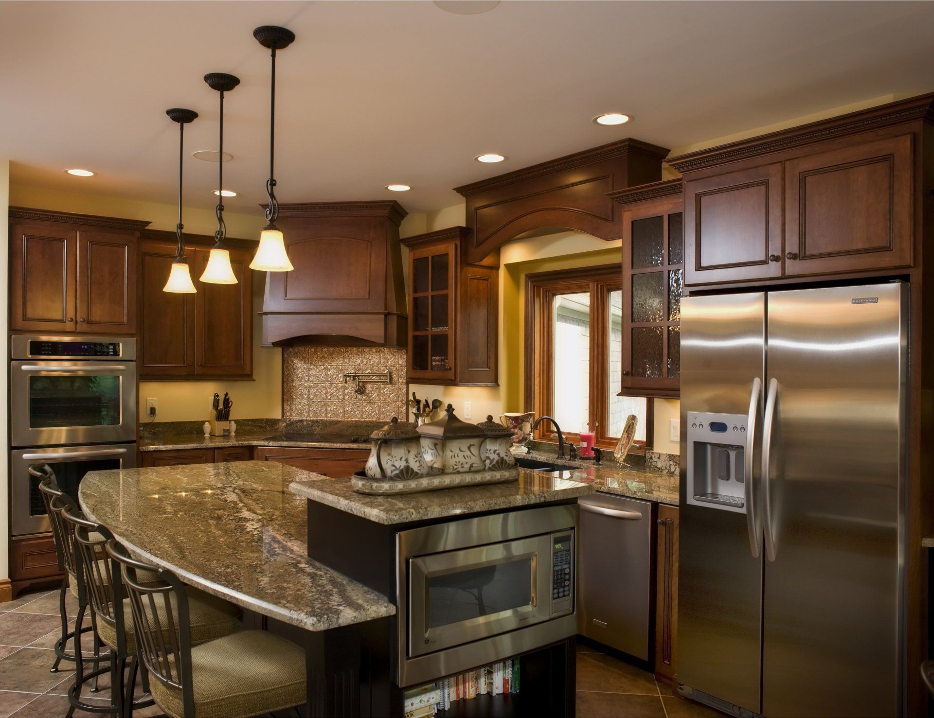 Kitchen with dark wood cabinets, granite countertops, stainless steel appliances, and island with pendant lights.