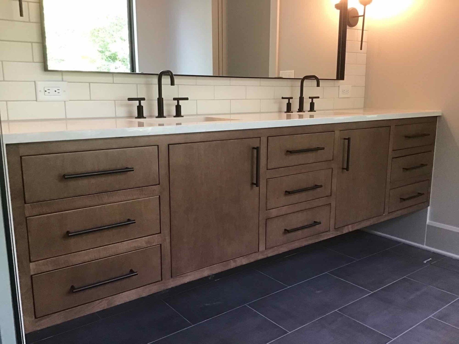 Modern bathroom with floating wooden vanity, white countertop, black fixtures, and blue tile floor.