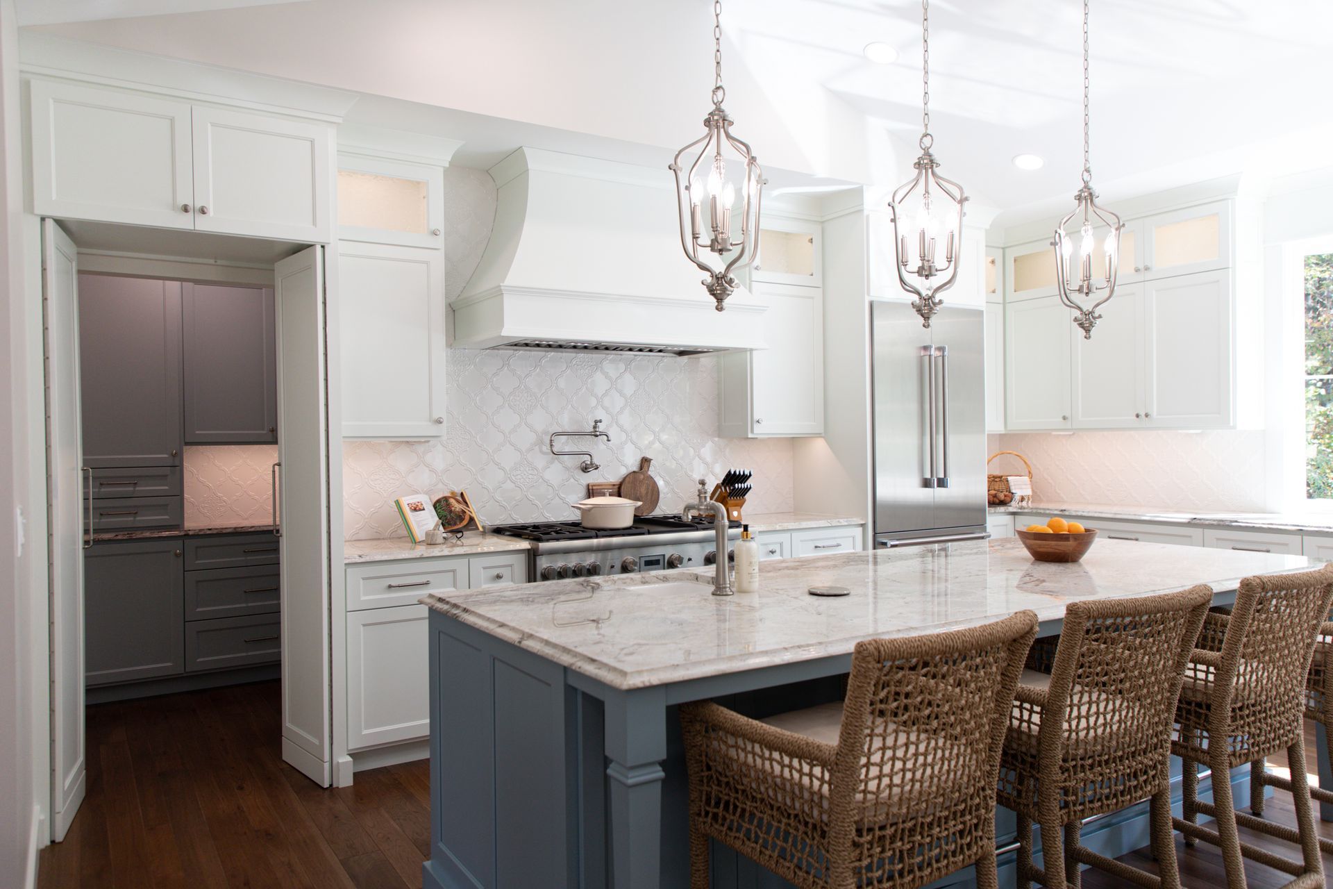 Bright white kitchen with a blue island and rattan bar stools.