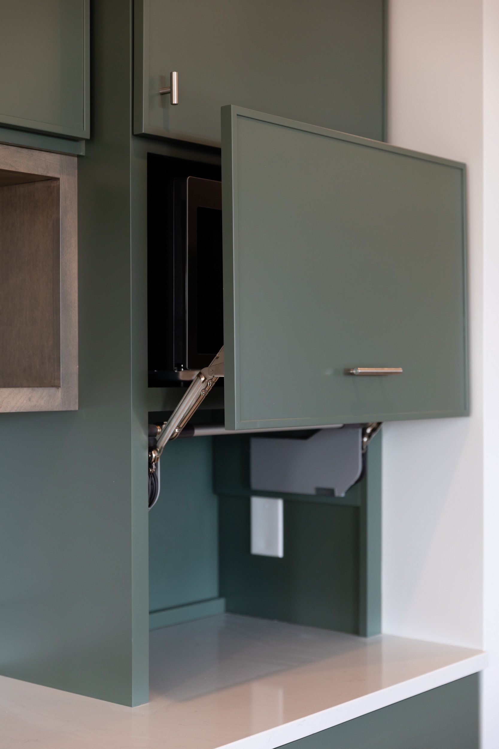 A green cabinet with a microwave inside of it.
