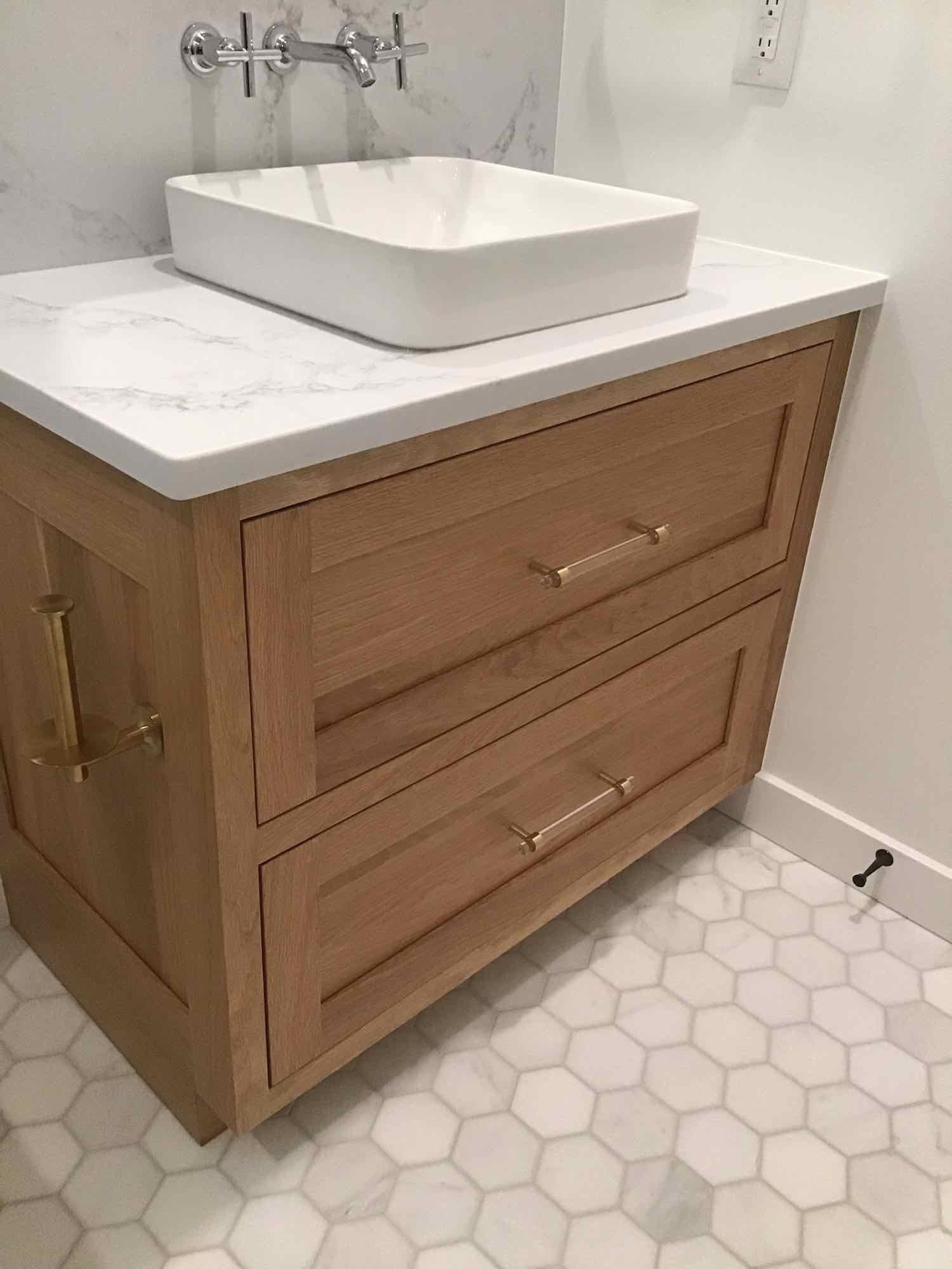 Light wood bathroom vanity with a white countertop and rectangular sink. Hexagon tile floor.