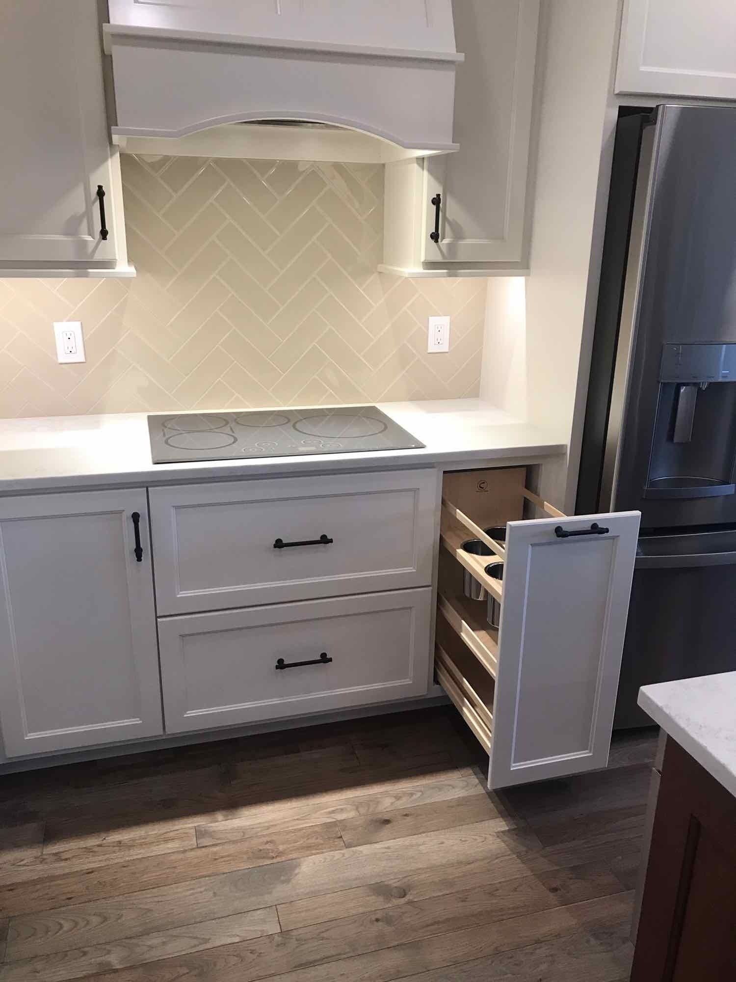 A kitchen with white cabinets, a stove, a refrigerator, and a pull out drawer.