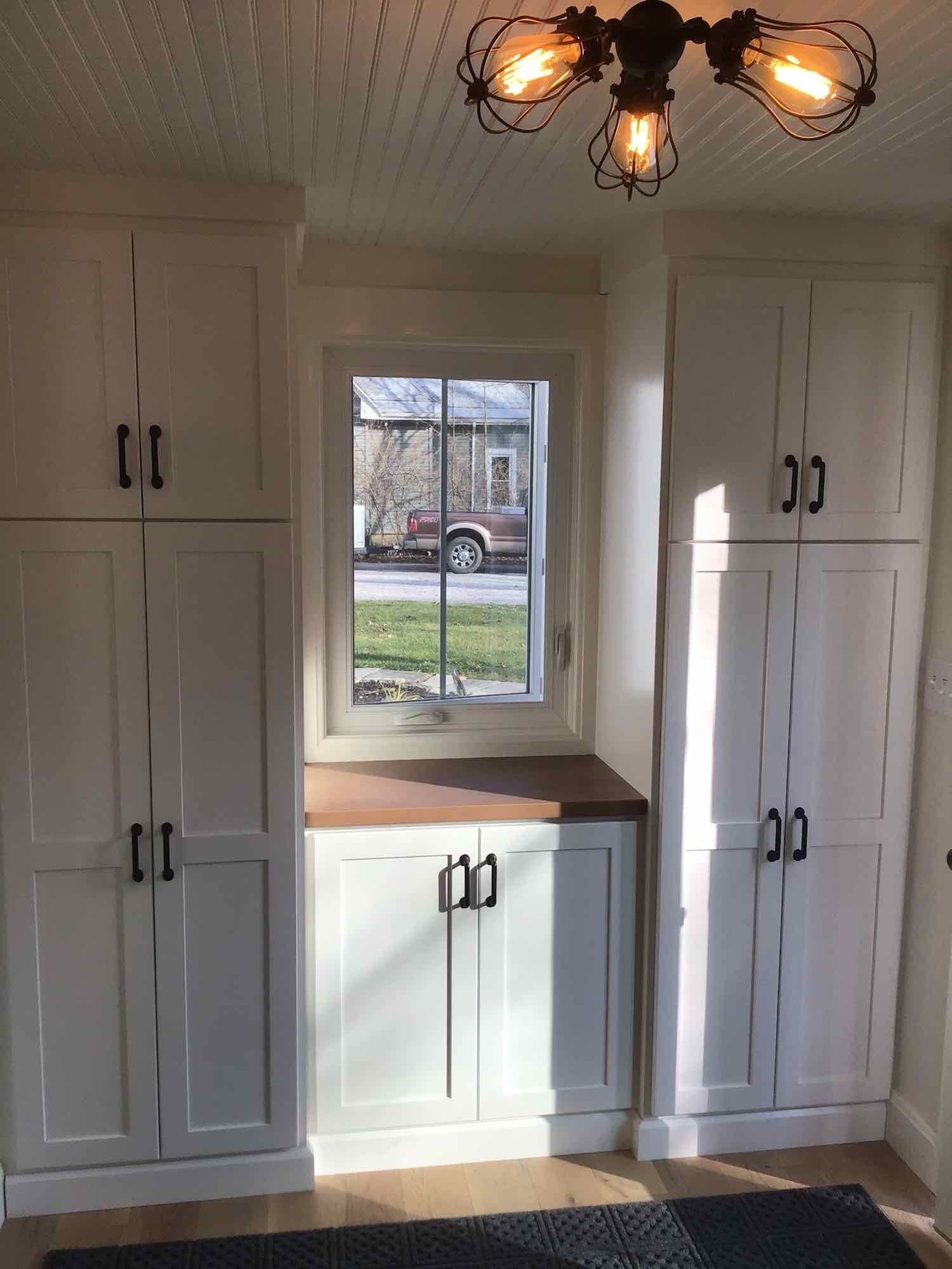 White kitchen cabinets flank a window, with a wooden countertop below. Black hardware and light fixture.
