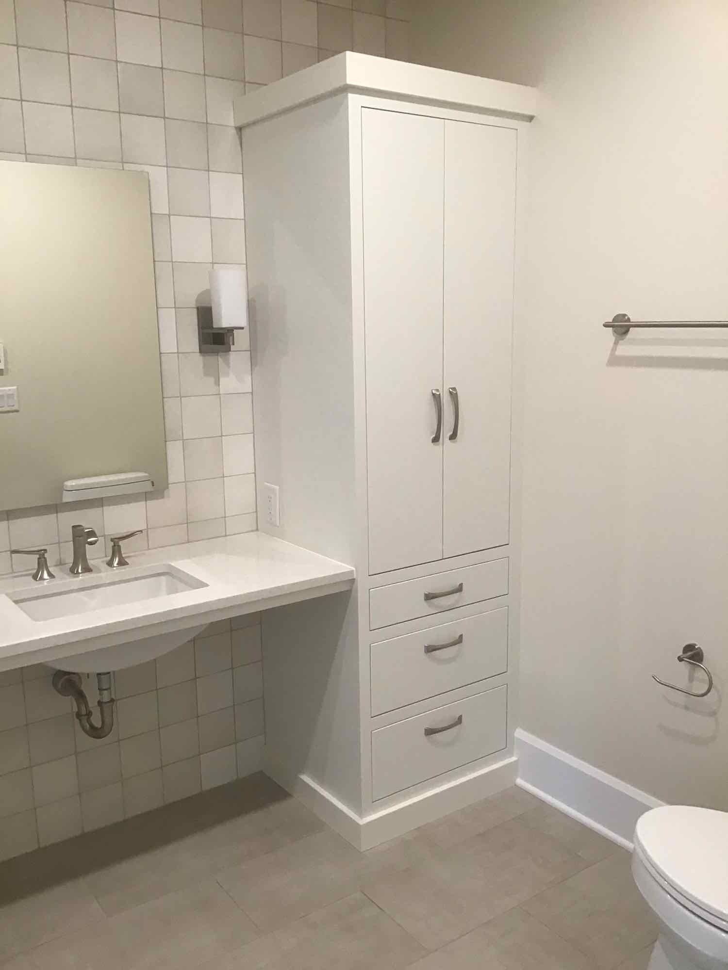 White bathroom with a tall storage cabinet, sink, toilet, and towel rack.