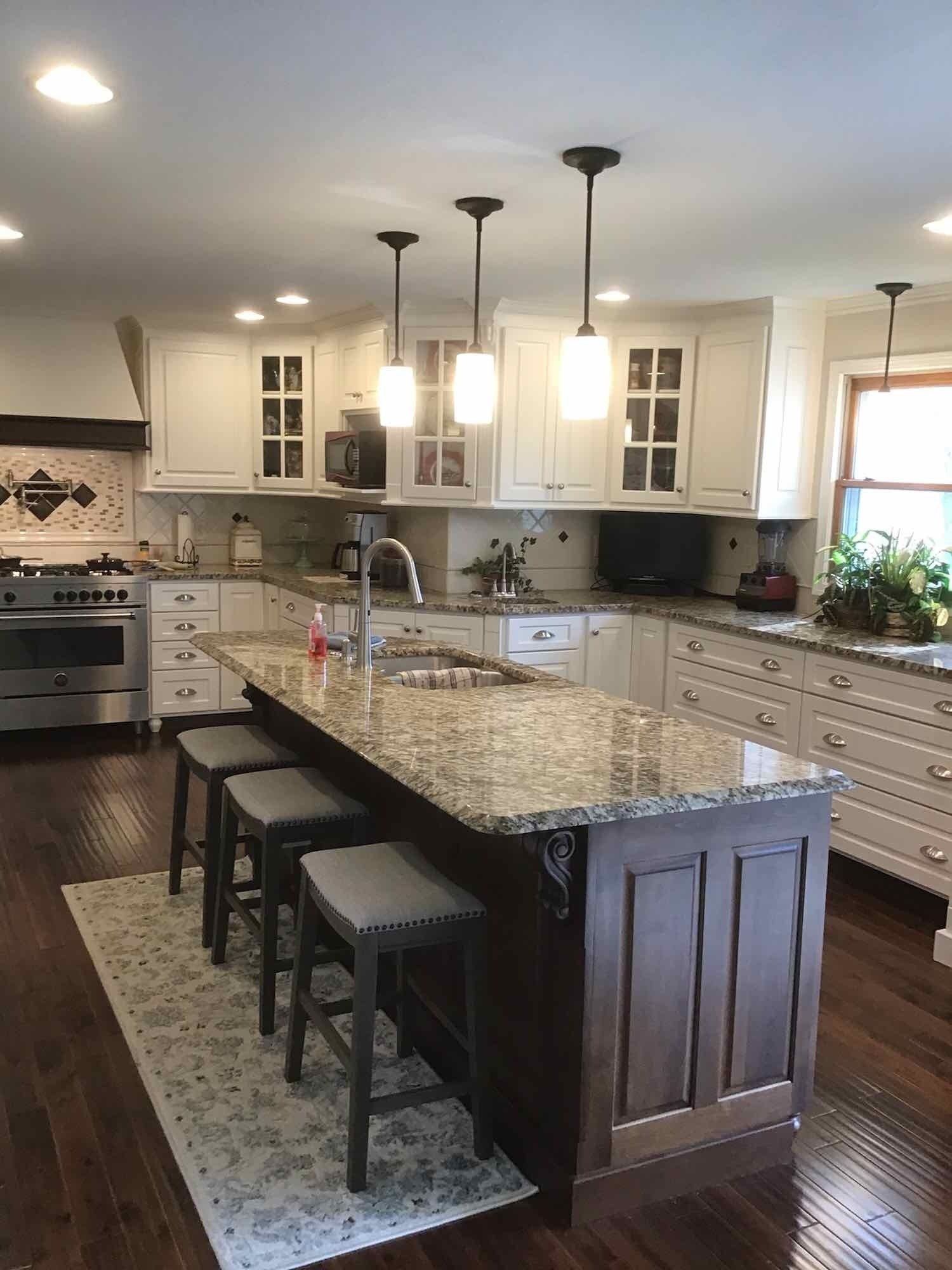 Kitchen with white cabinets, dark island with seating, granite countertop, and pendant lights.