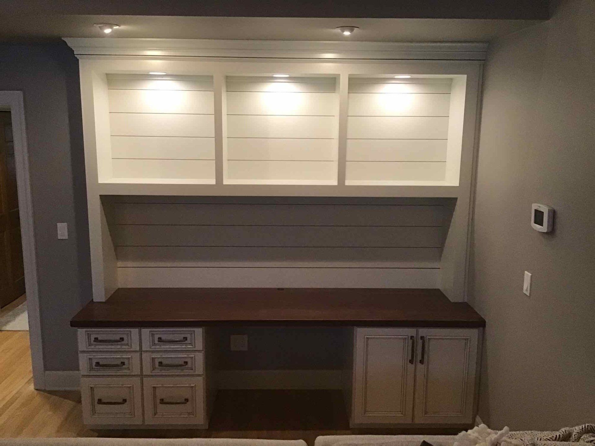 Built-in desk with overhead shelves, white with wood top and distressed white cabinets.