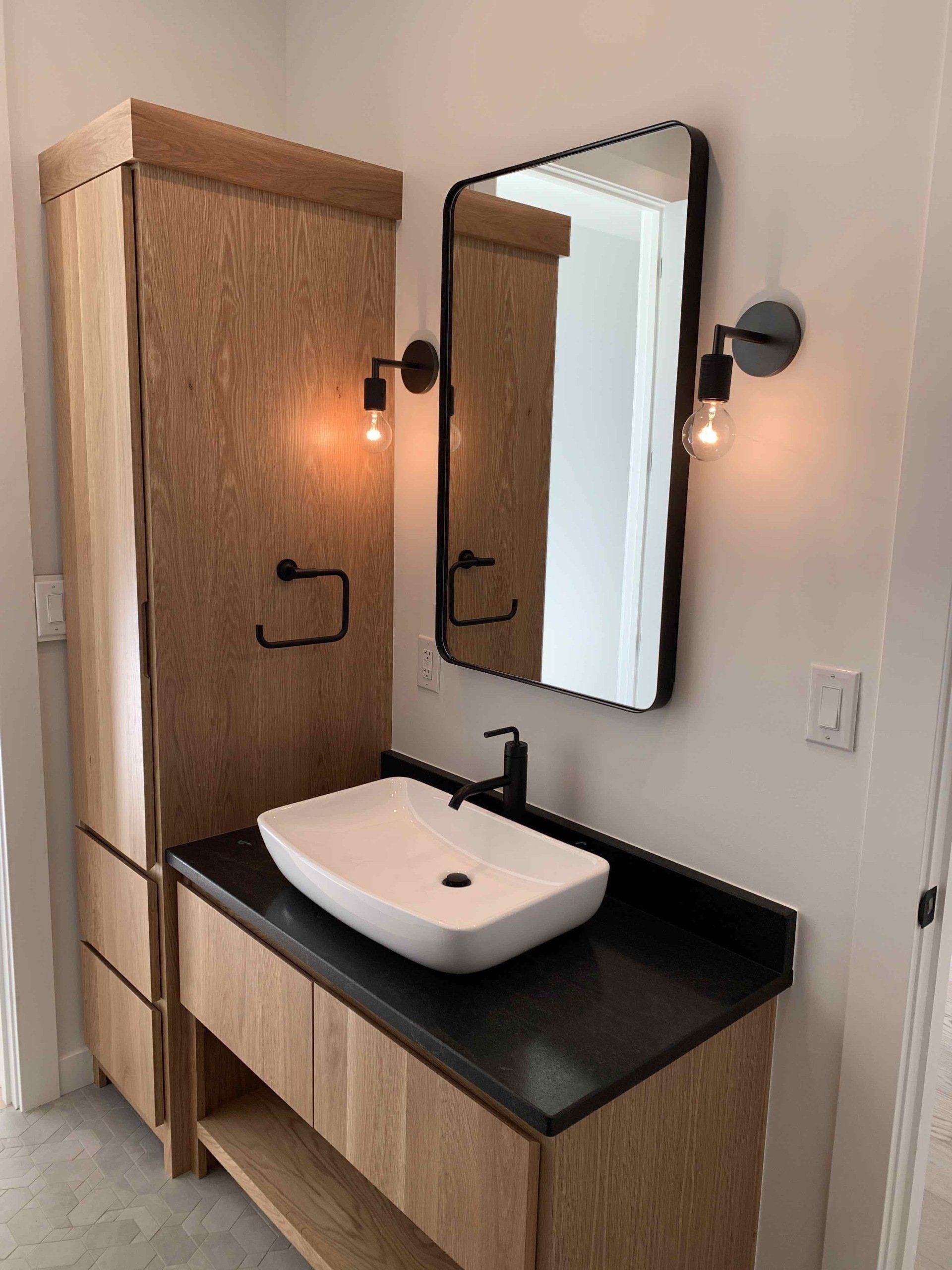 Bathroom with wooden cabinetry, black countertop, vessel sink, mirror, and sconces.