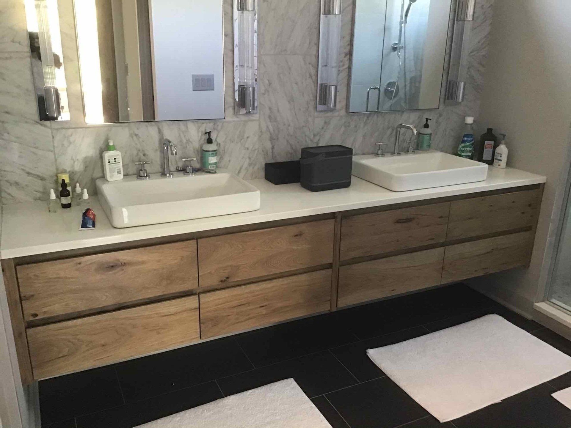 Floating wood vanity with two sinks, mirrors, and white towels in a modern bathroom.