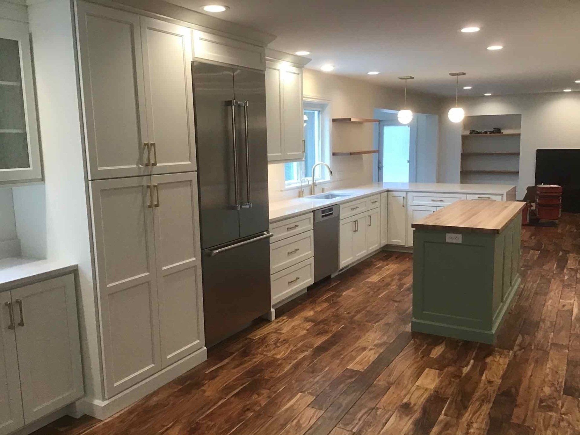 Modern kitchen with white cabinets, stainless steel refrigerator, and green island. Wooden floors.