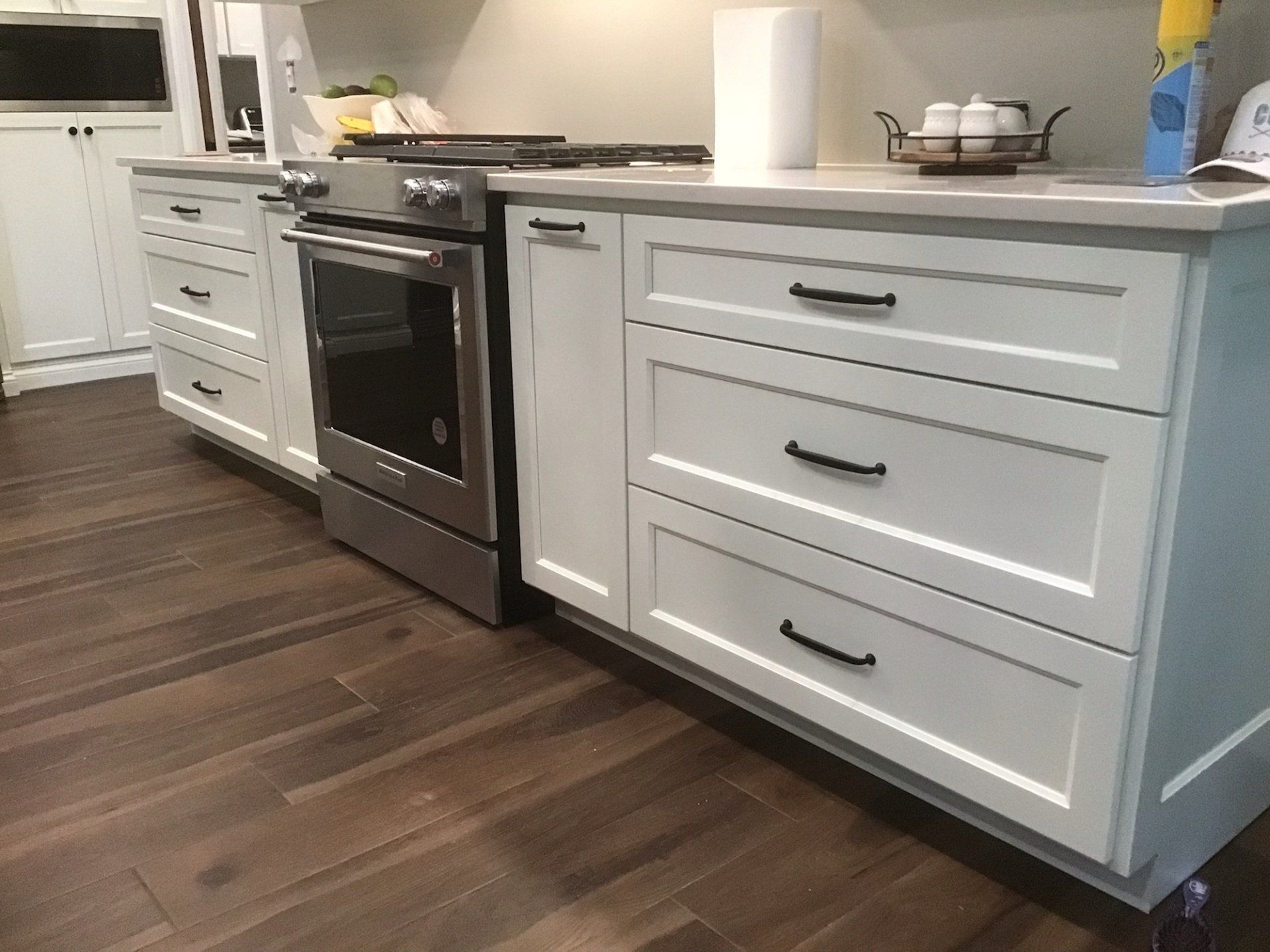 White kitchen cabinets with black handles, a stove, and wood flooring.
