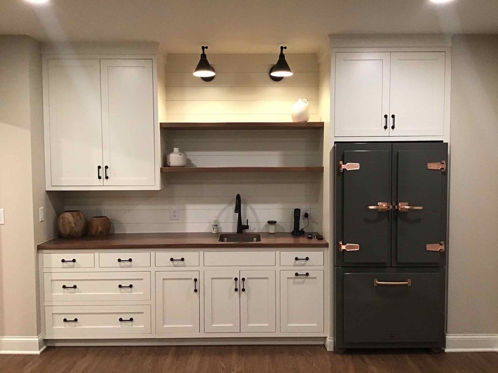White and wood-toned wet bar with dark appliances, cabinets, shelving, and black fixtures.