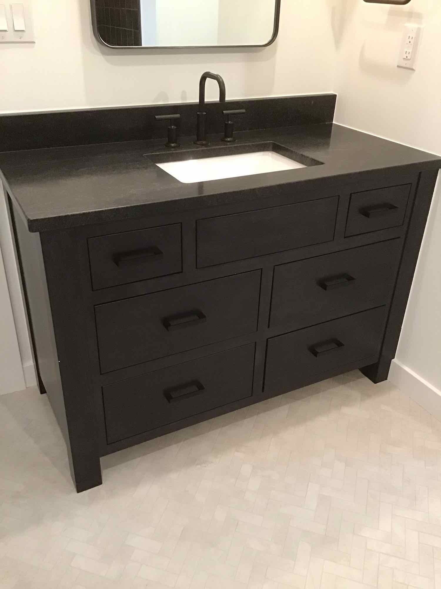 Black bathroom vanity with drawers and a sink, set against a white-tiled floor.