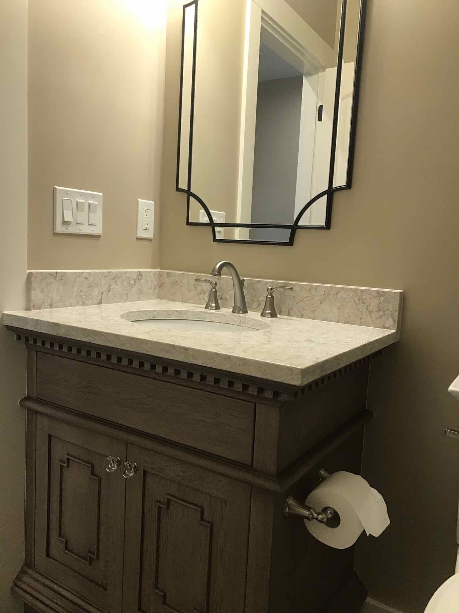 Bathroom vanity with gray cabinet, white countertop, silver faucet, and decorative black mirror frame.