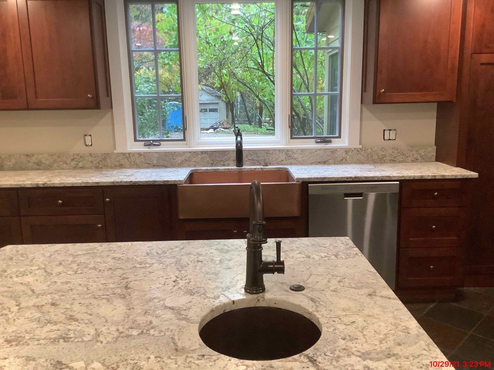 Kitchen with granite countertops, brown cabinets, copper sink, and view of trees.