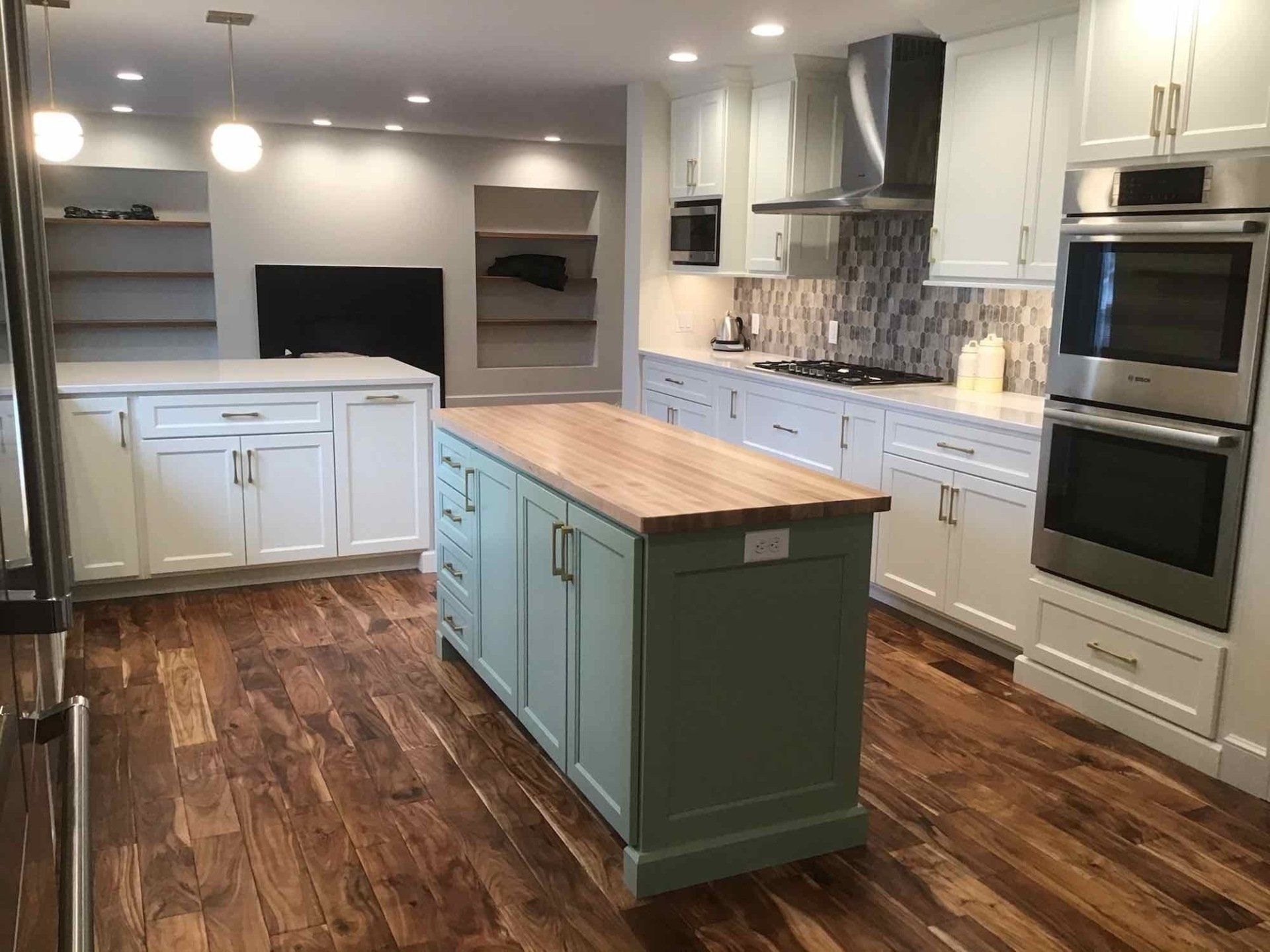 Modern kitchen with wooden floors, two islands, white cabinets, and stainless steel appliances.