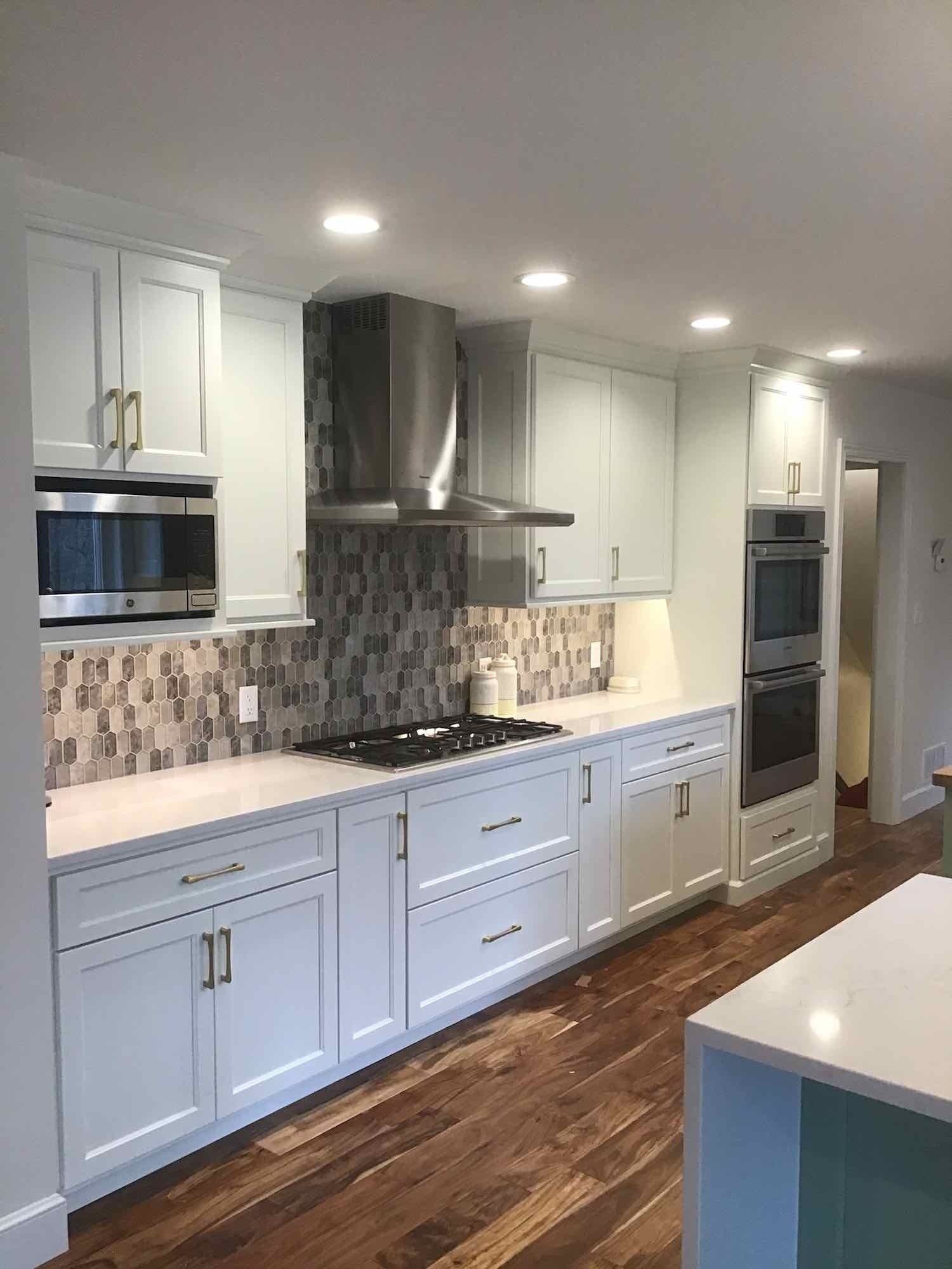 White kitchen with wood floor, stainless steel appliances, and backsplash.