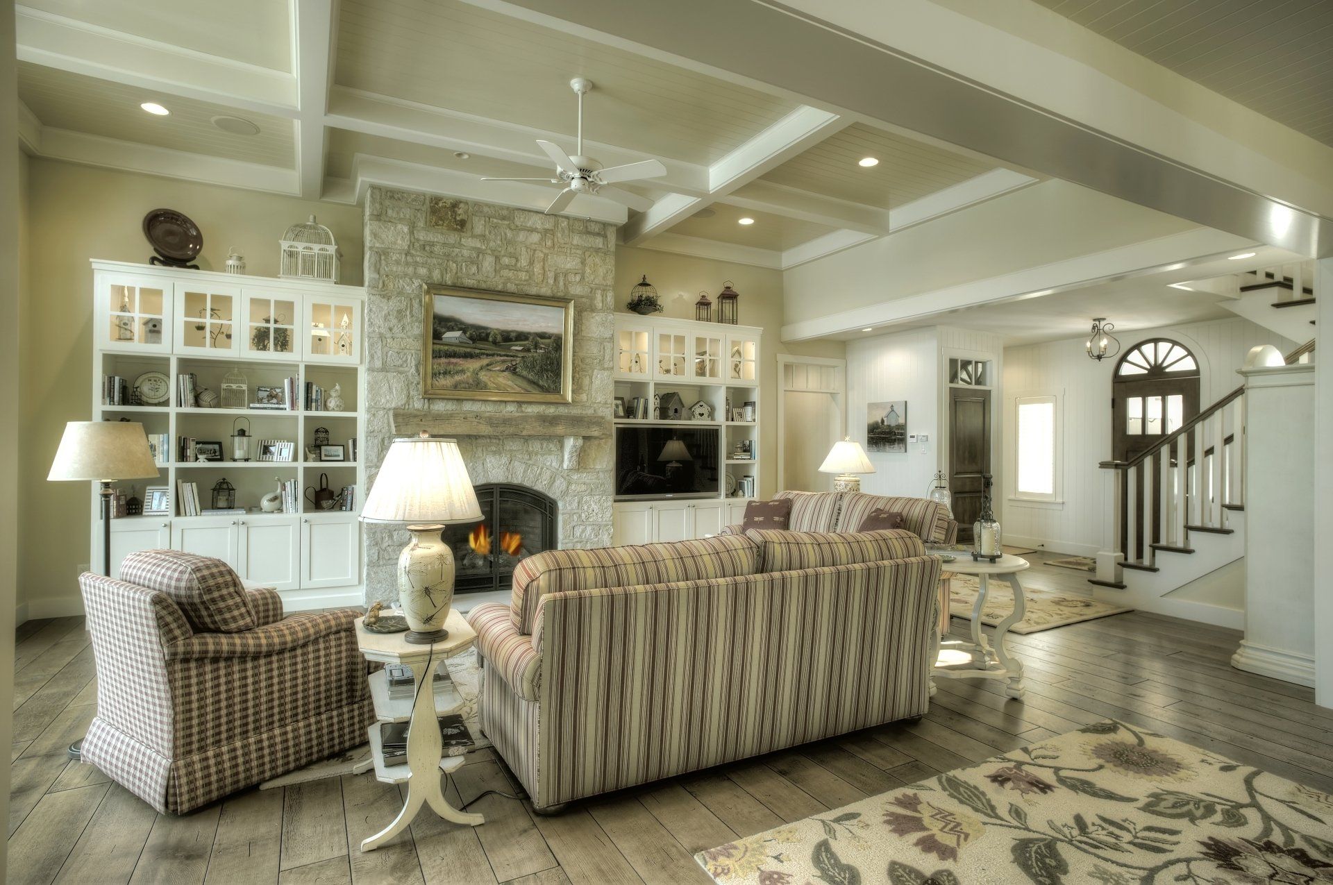 Living room with stone fireplace, built-in shelves, patterned sofa, and hardwood floors.