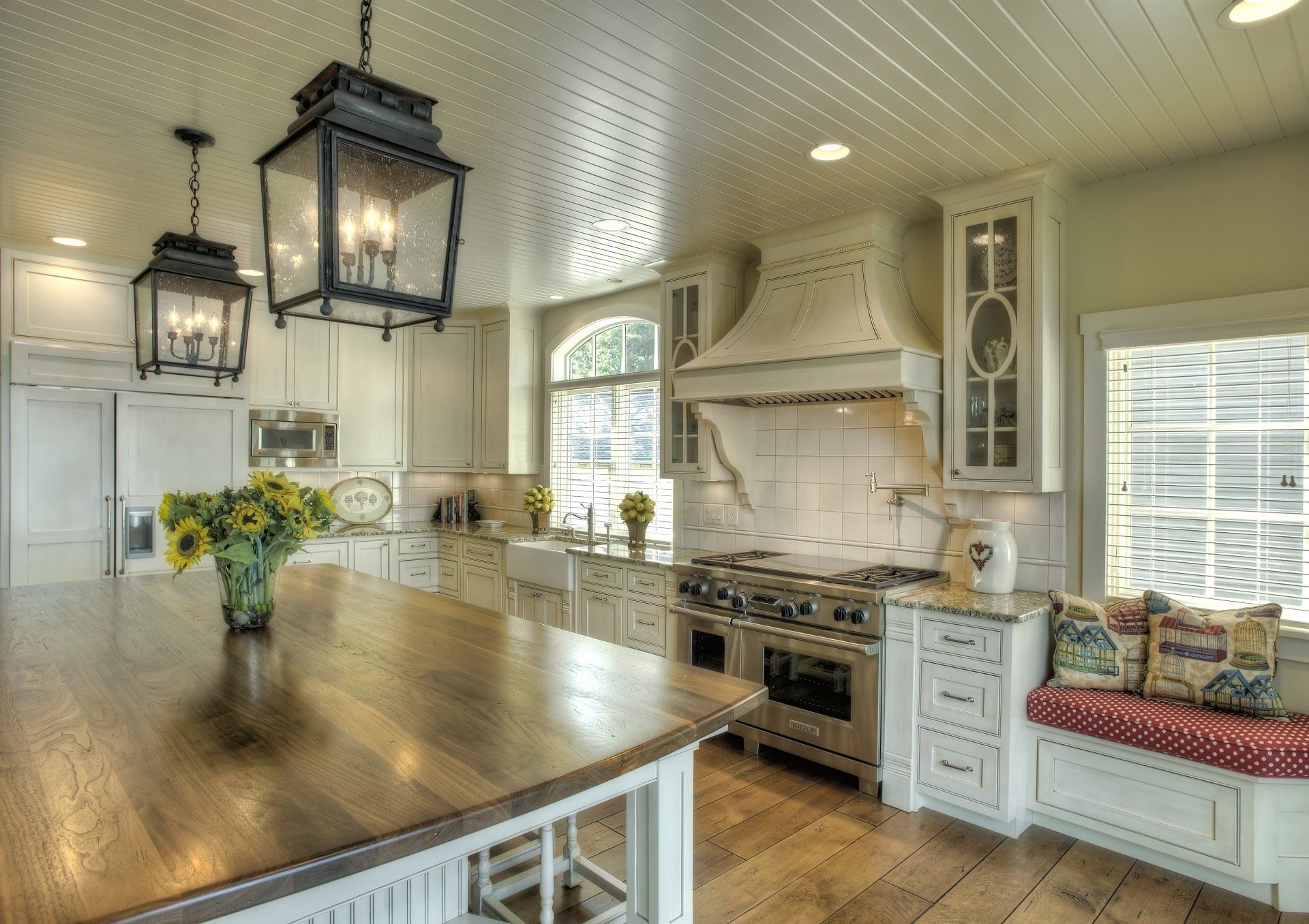 Kitchen with wooden island, white cabinetry, lantern lights, and range.