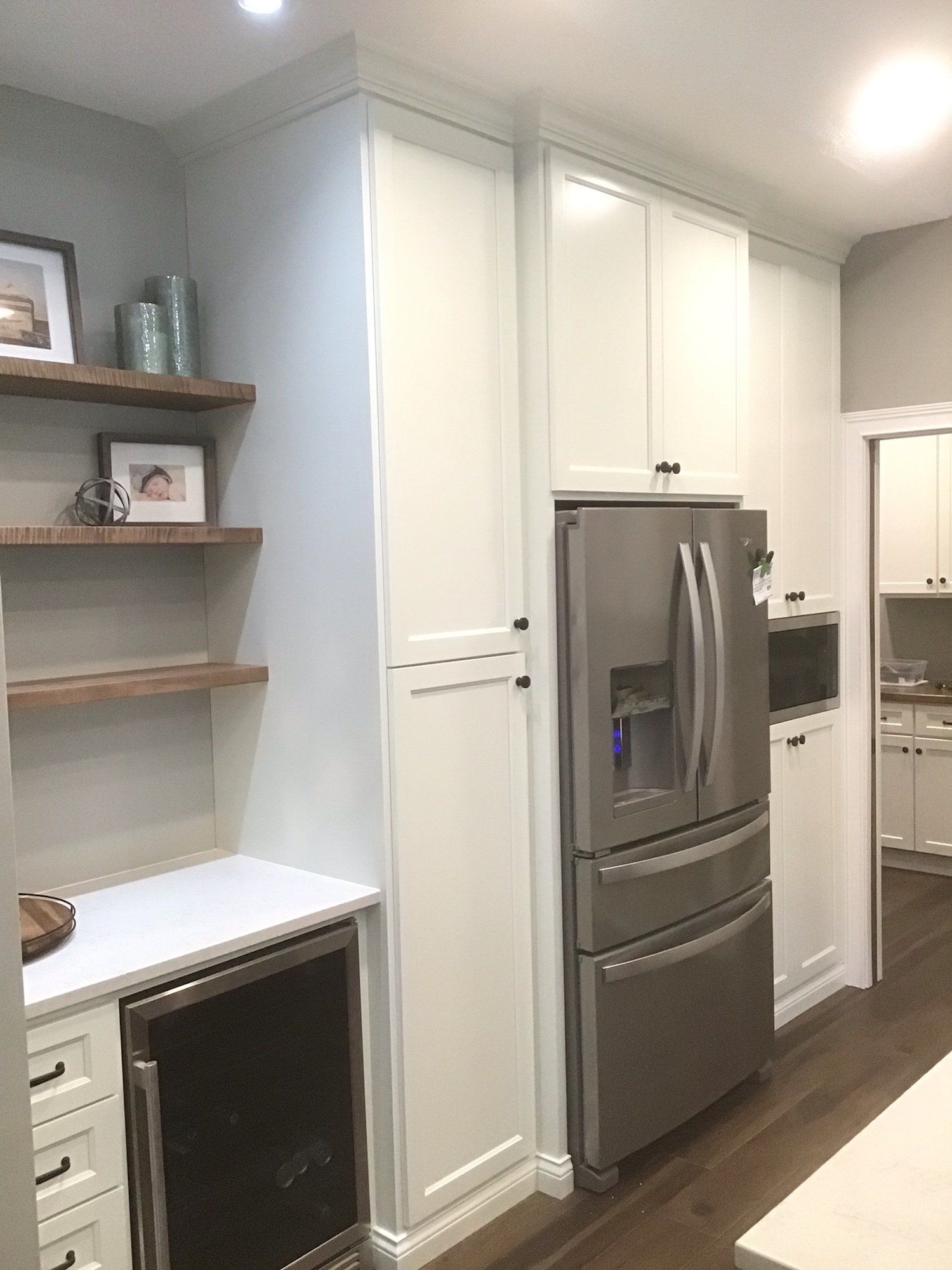 Kitchen with white cabinets, stainless steel refrigerator, wine cooler, and open shelving.