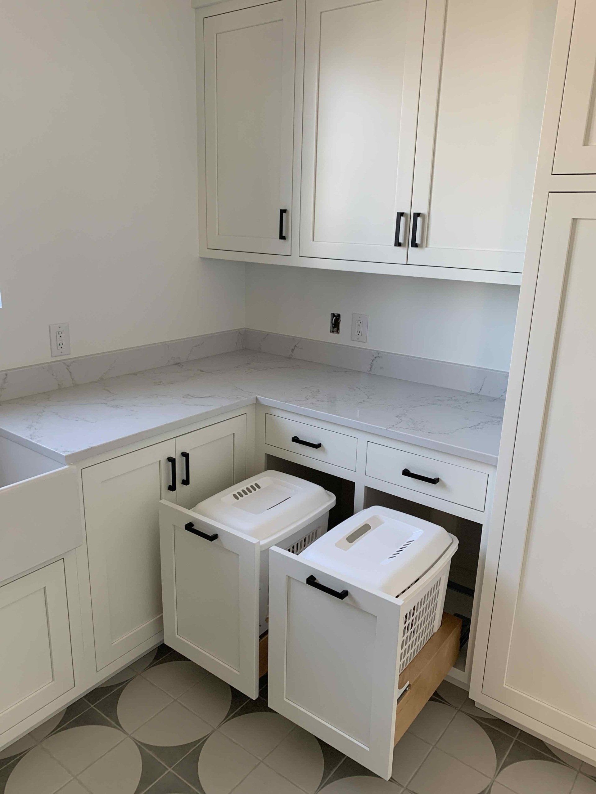 A laundry room with white cabinets and drawers and a sink.