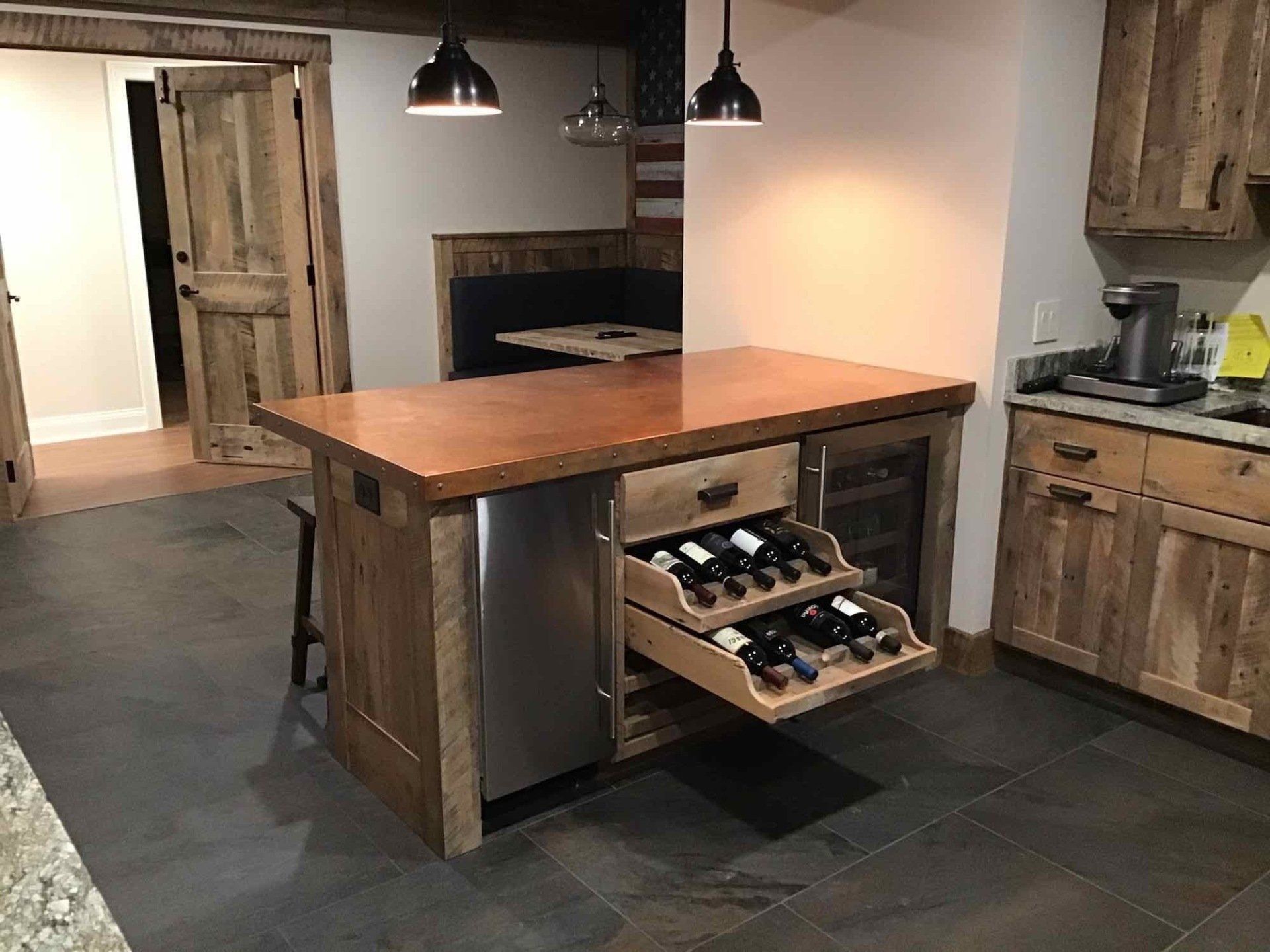 A kitchen with a wooden island and drawers filled with wine bottles.