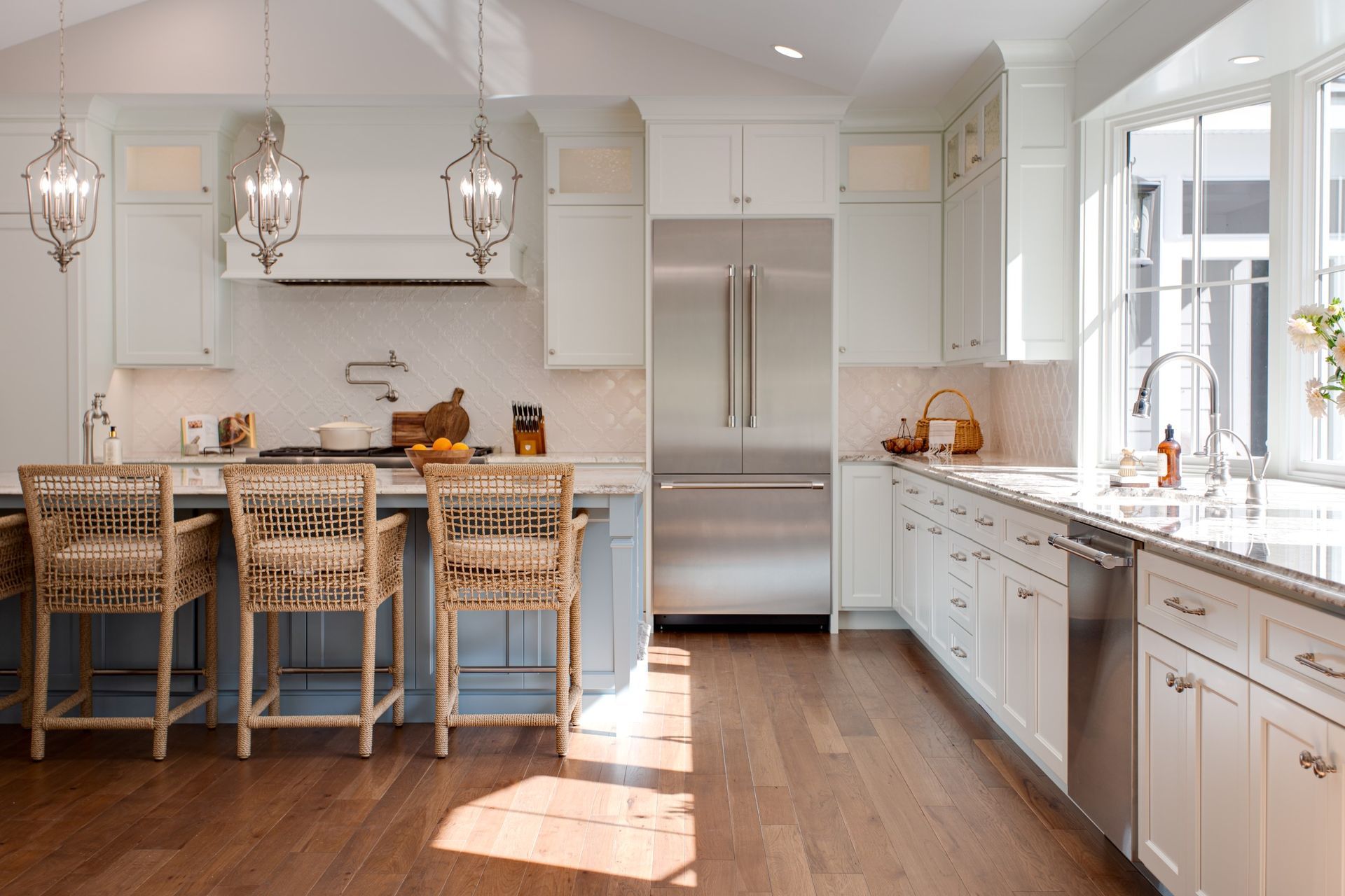 Elegant white kitchen with blue island, stainless steel appliances, and wood floors.