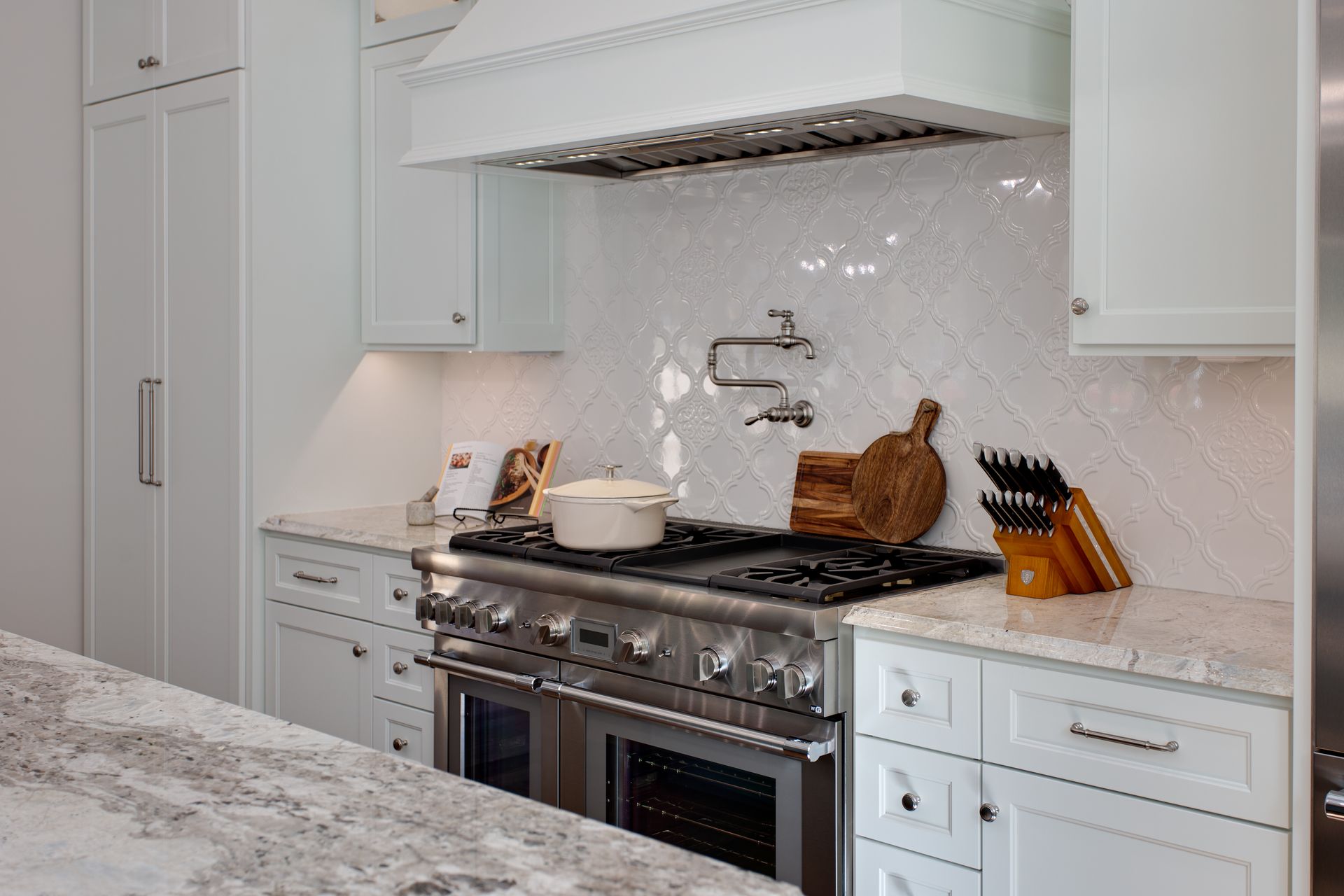 White kitchen with stove, range hood, cabinets, and granite countertops.