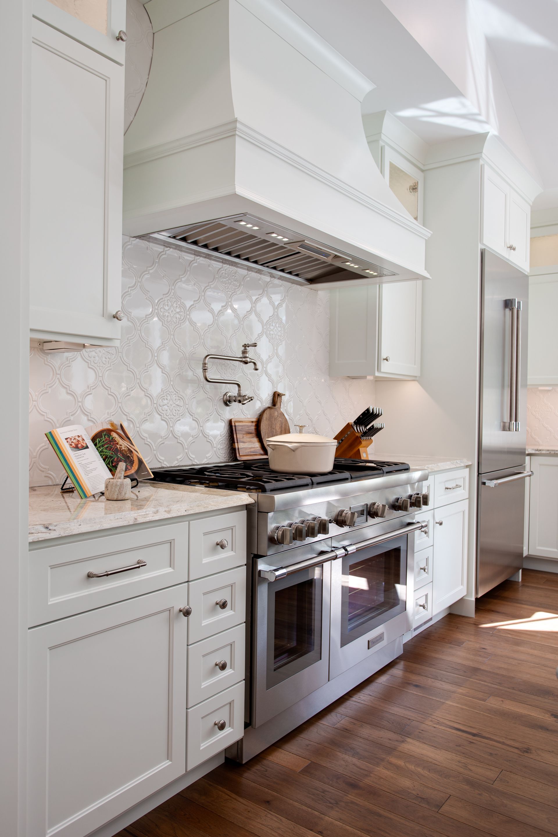 White kitchen with stainless steel oven, hood, and cabinetry; wood floor.