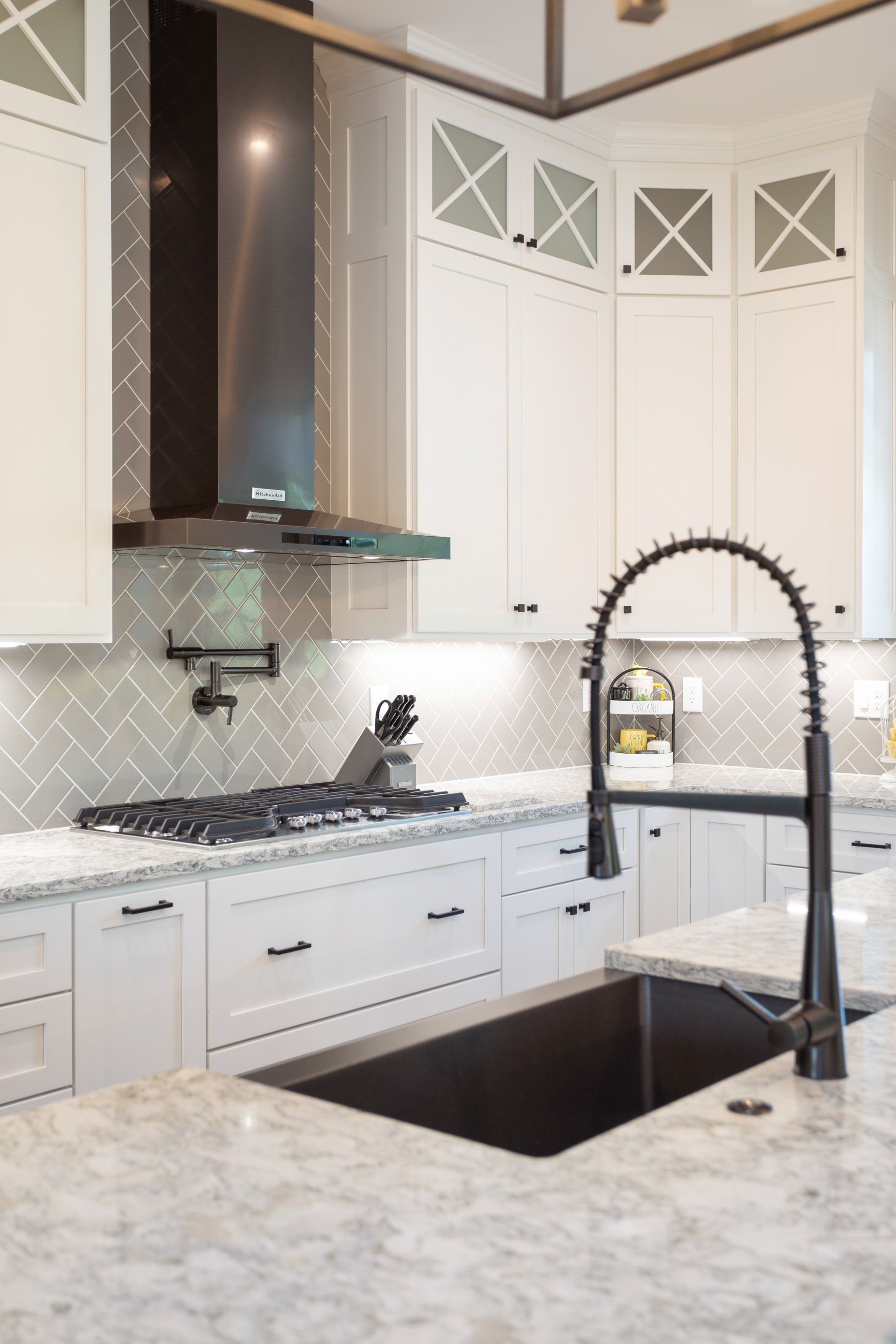 Modern white kitchen with stainless steel appliances, black sink, and herringbone backsplash.