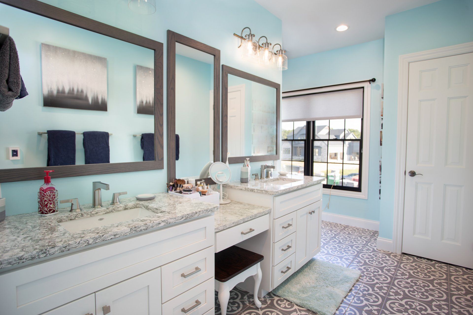 Bathroom with light blue walls, white vanities, gray countertops, and patterned floor.