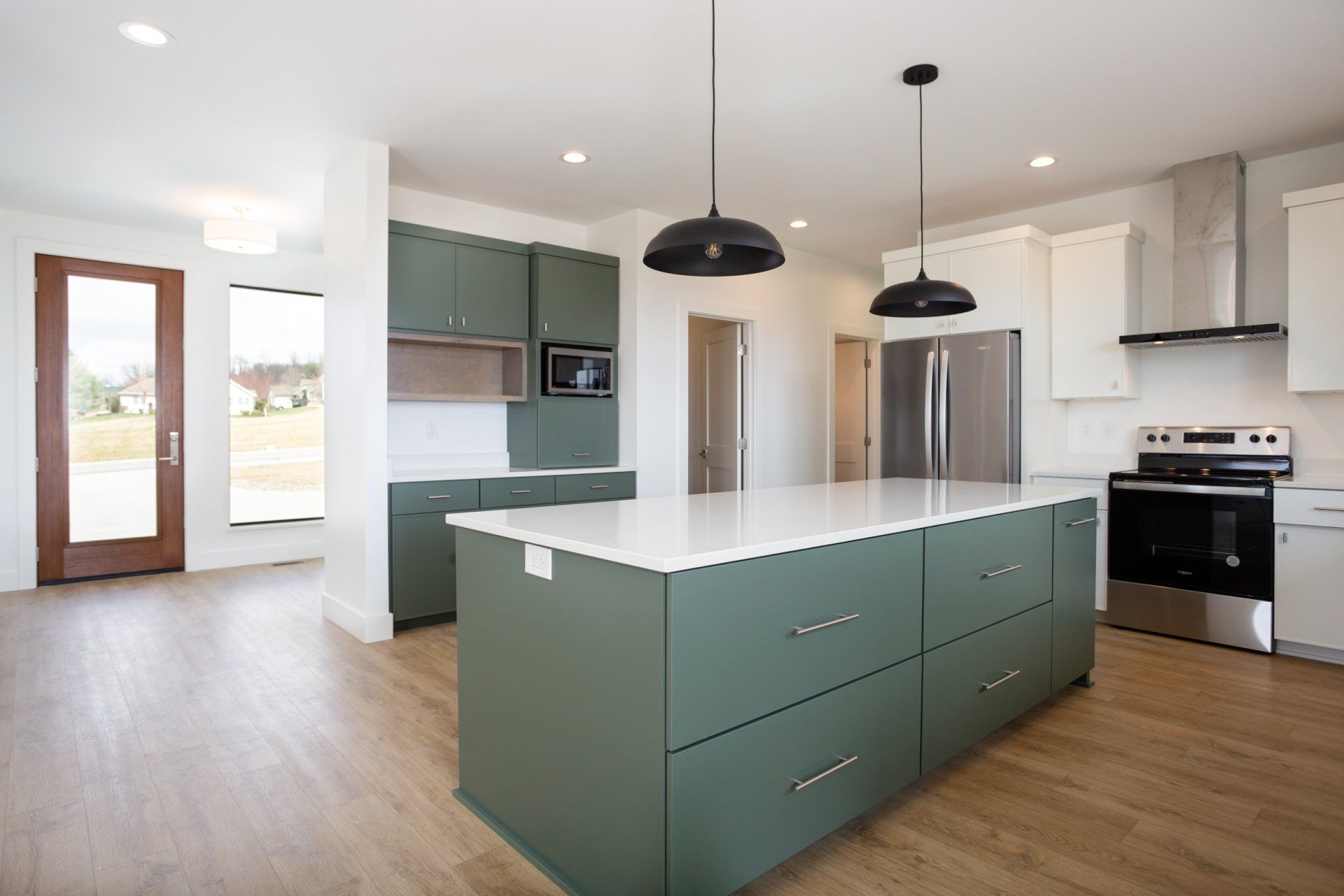 Spacious modern kitchen with olive-green island and cabinets, stainless steel appliances, and white countertops.