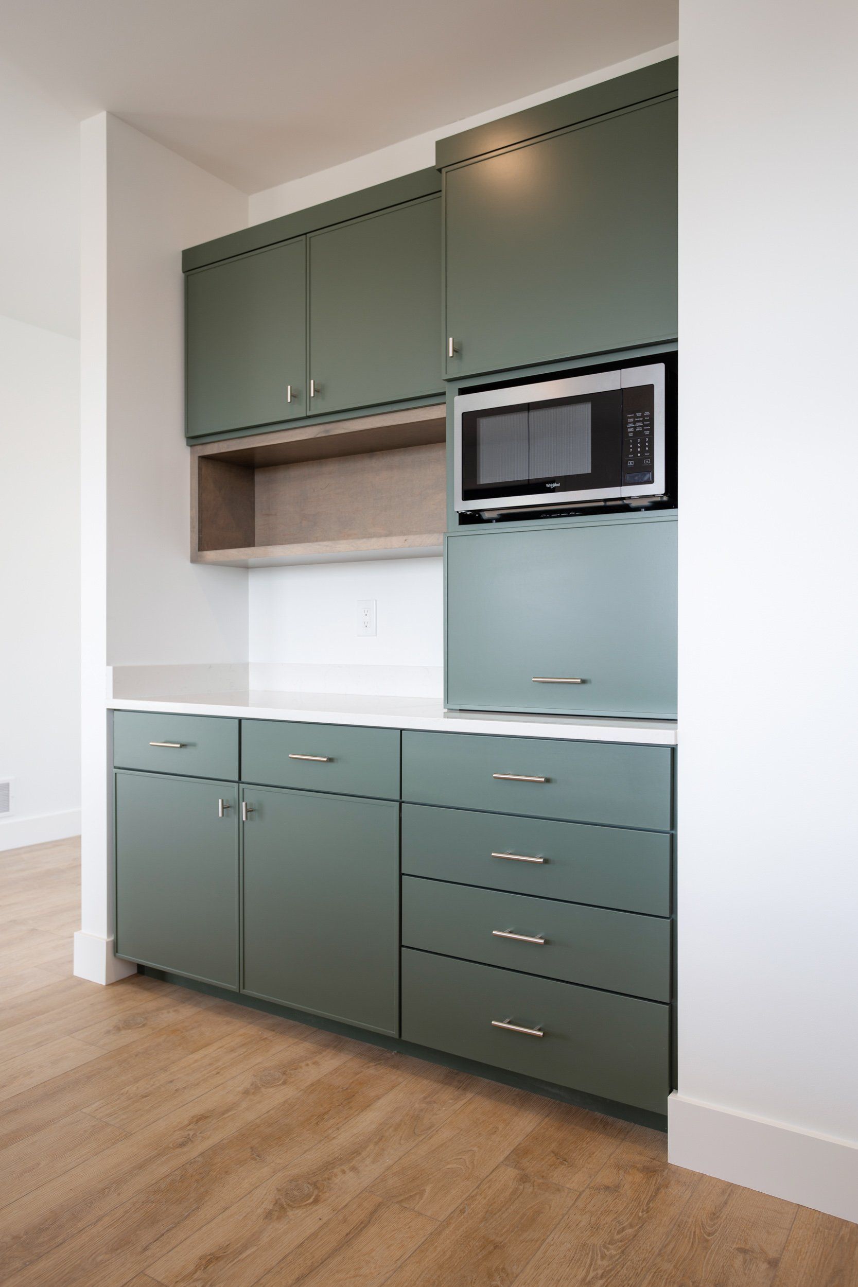 Green kitchen cabinets with a microwave and light wood flooring.