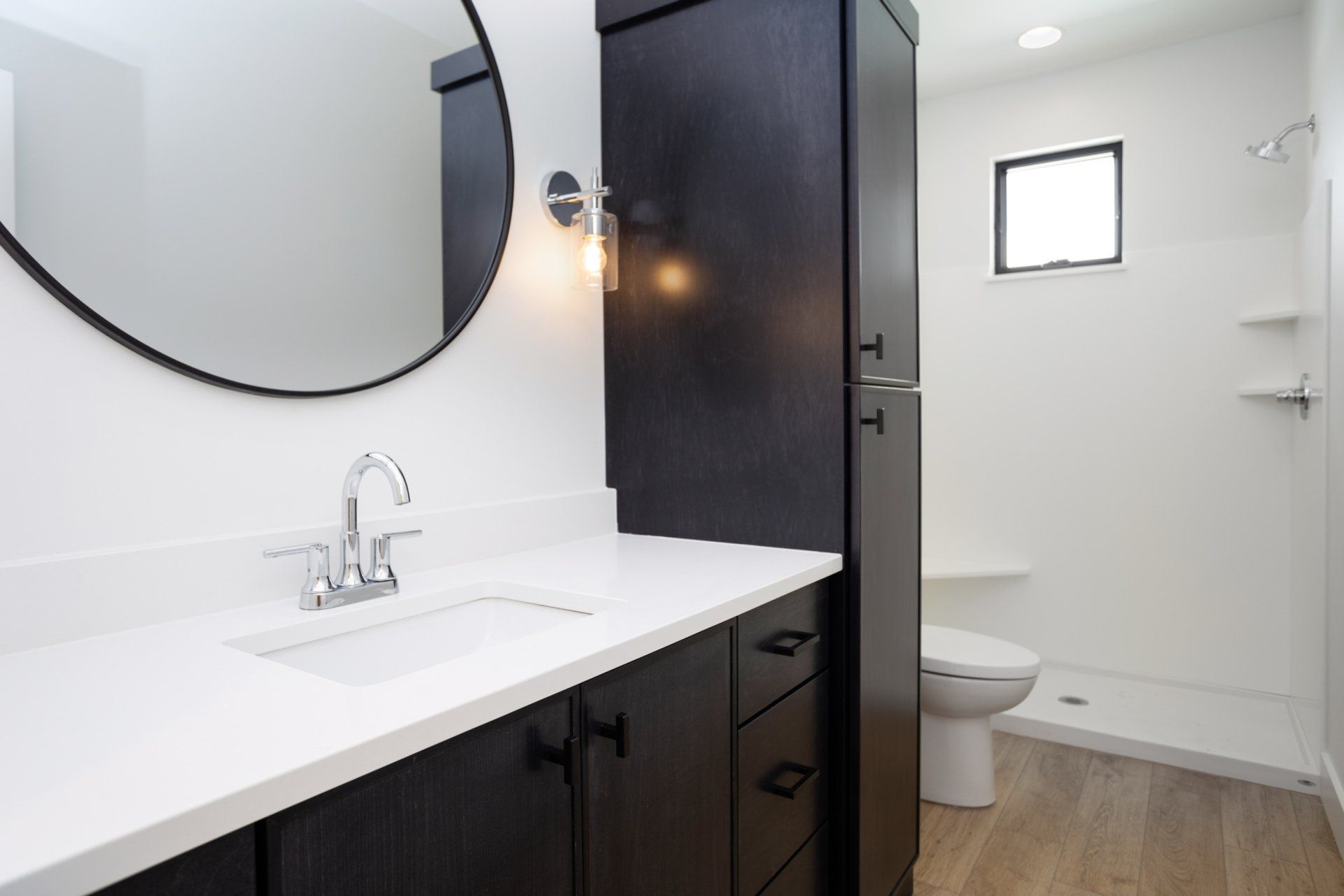 Bathroom with a white countertop, black cabinets, and a round mirror.
