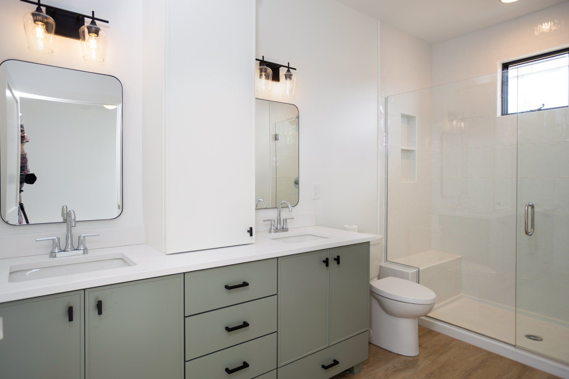 Modern bathroom with sage green vanity, two mirrors, and a glass shower.