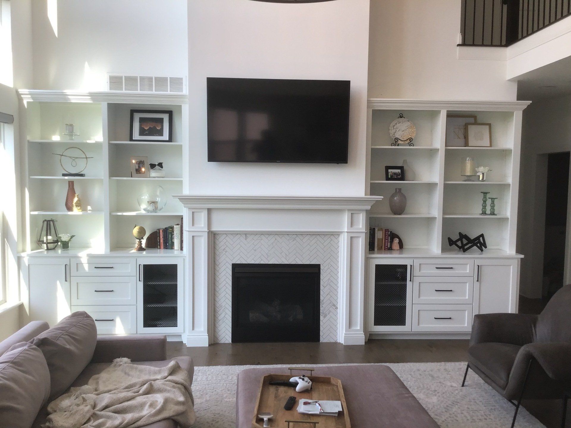 Living room with fireplace, white built-in bookshelves, and large TV. A sectional sofa and armchair are in the foreground.