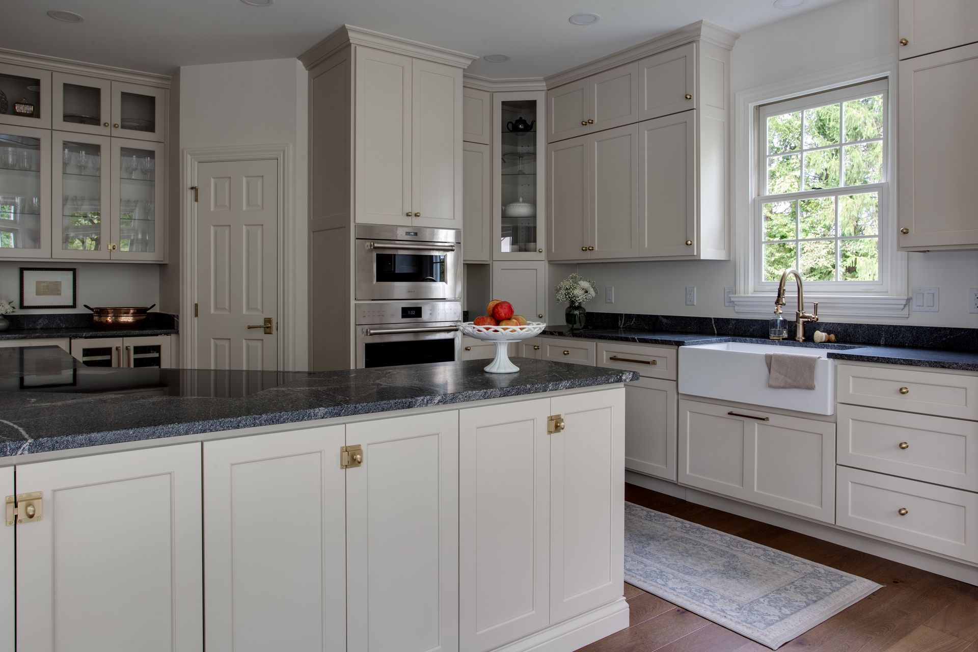 Elegant white kitchen with dark countertops, island, cabinets, and a window.