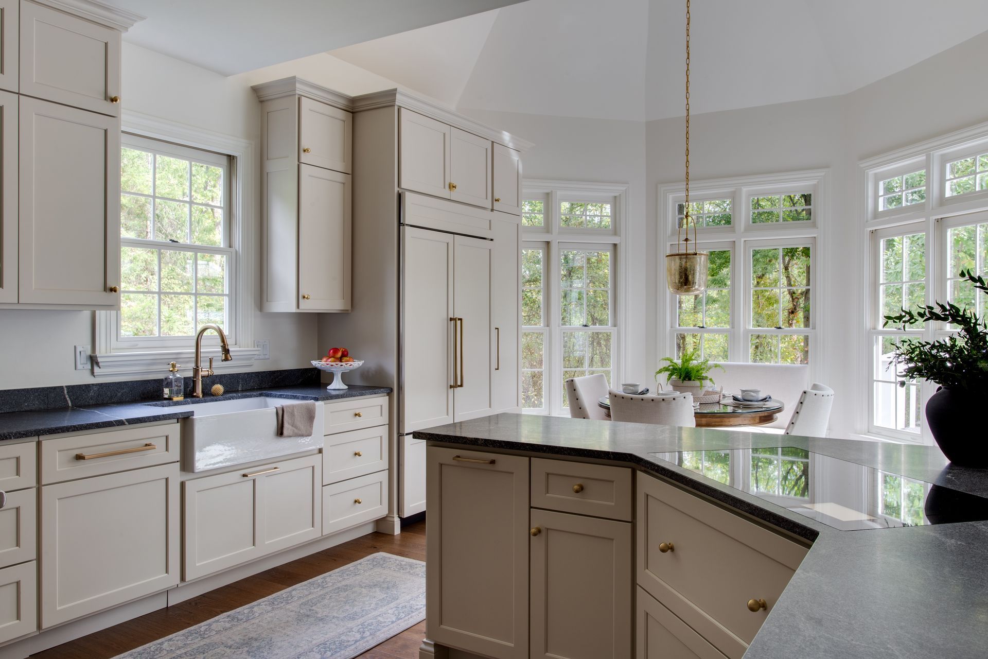Cream-colored kitchen with granite countertops, gold hardware, and bay windows overlooking greenery.