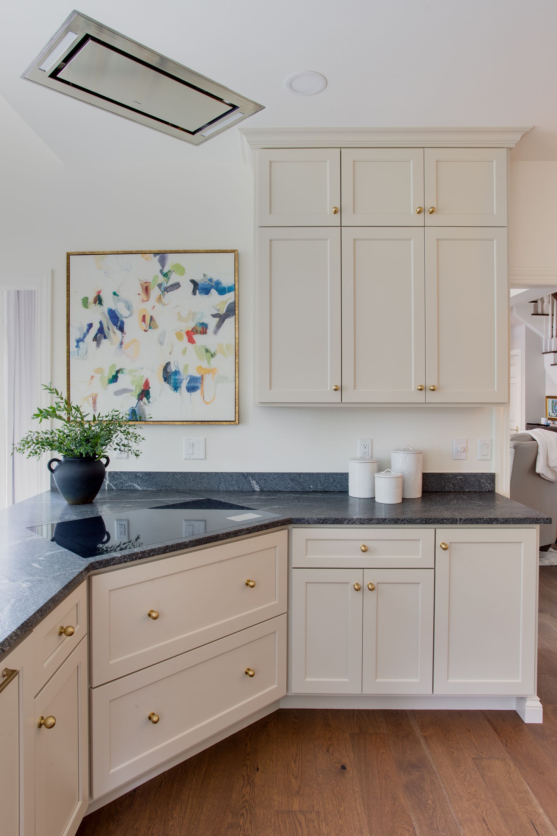 Cream-colored kitchen cabinets with black countertops and artwork. Dark wood floors.