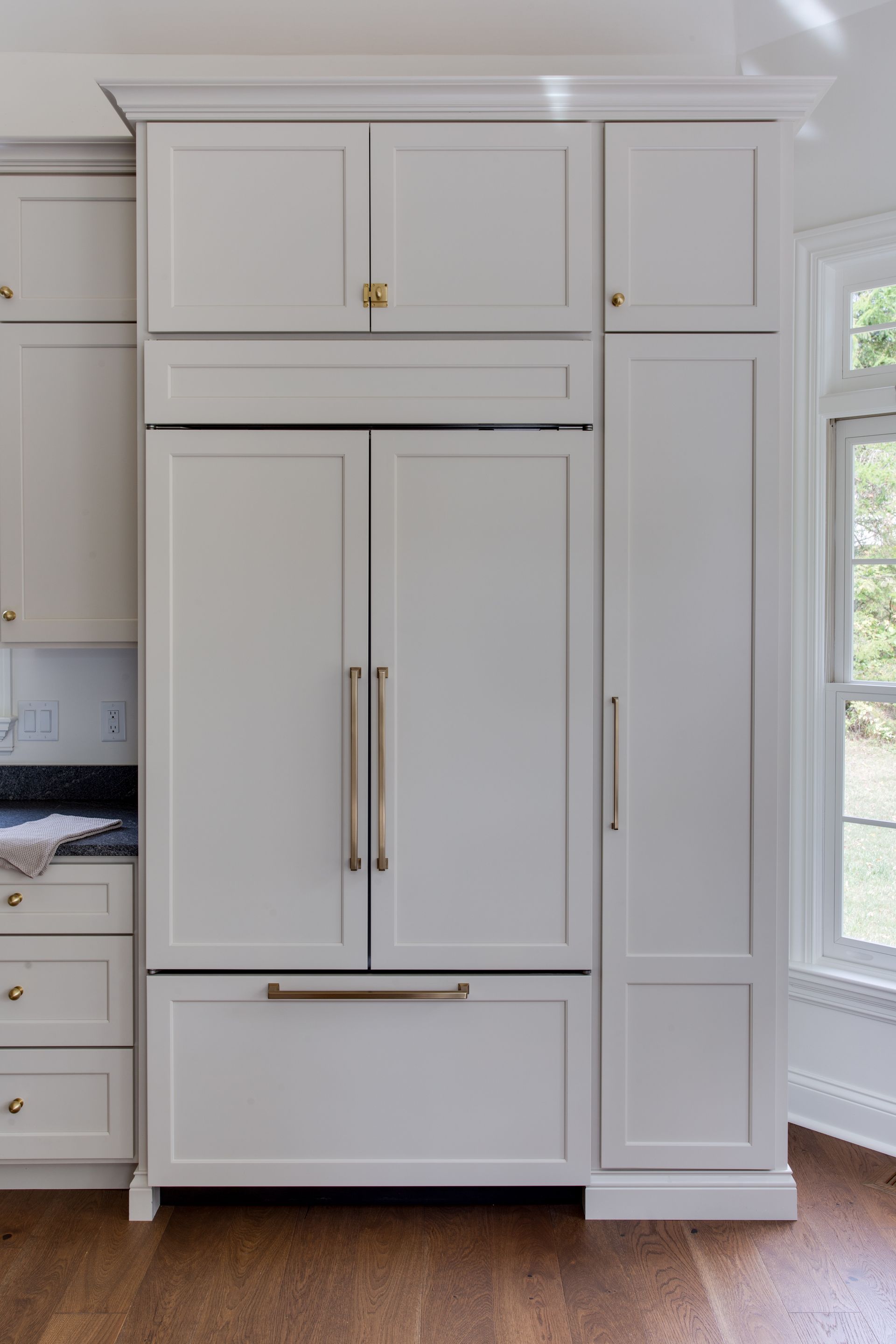 White built-in refrigerator and cabinetry with stainless steel handles, in a kitchen next to a window.
